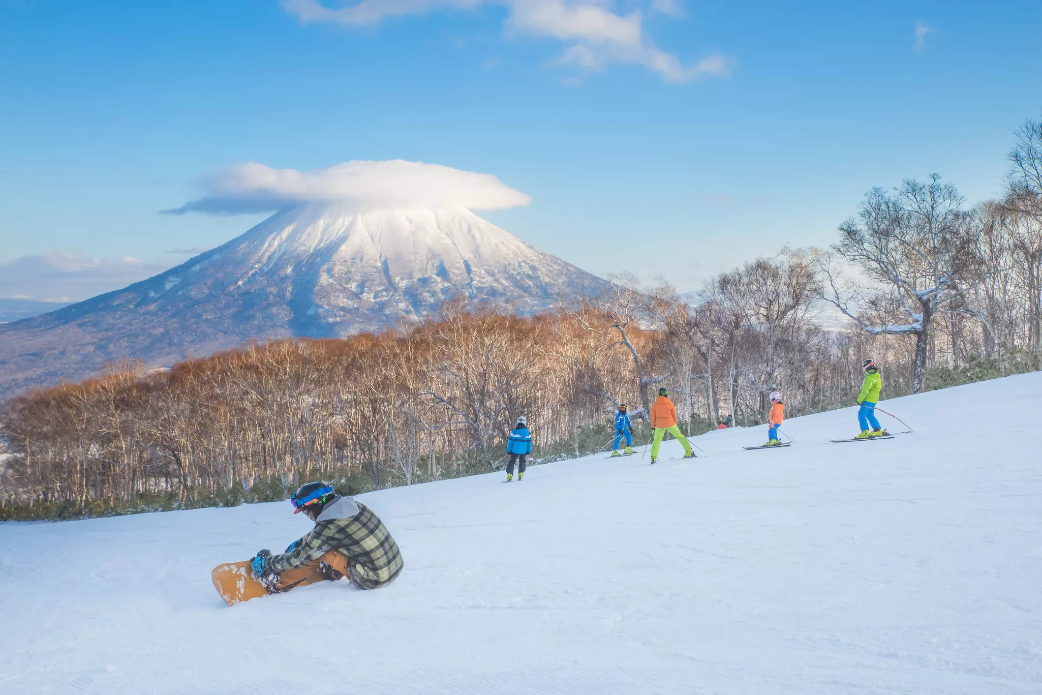 Snowboarders and skiiers on slopes in the shadow of a large mountain peak