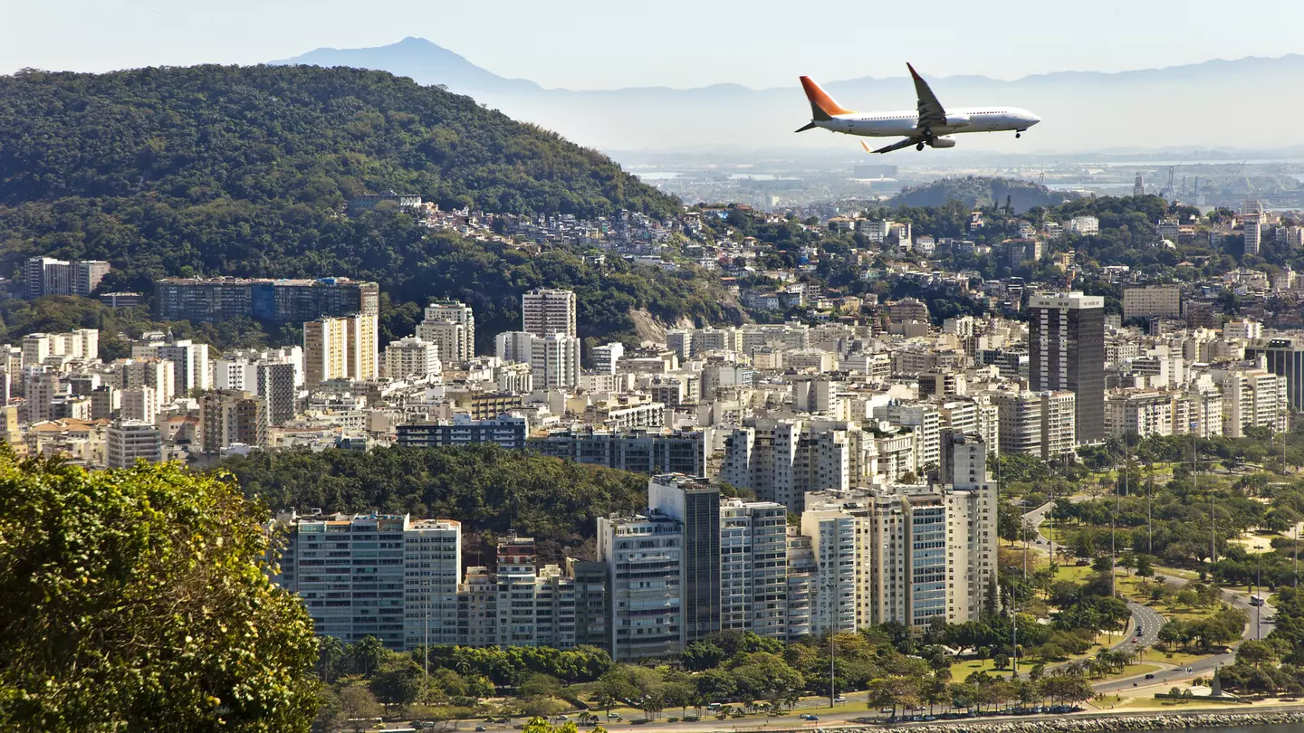 A commercial jet flies over a built-up city by the sea