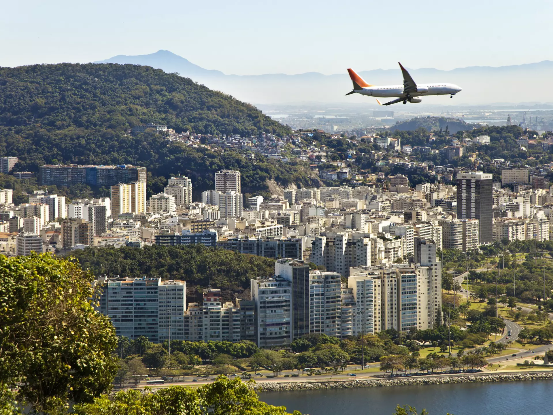A commercial jet flies over a built-up city by the sea
