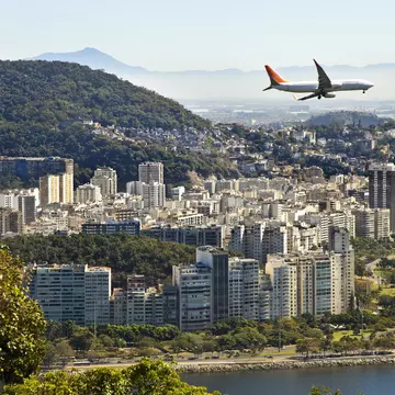 A commercial jet flies over a built-up city by the sea