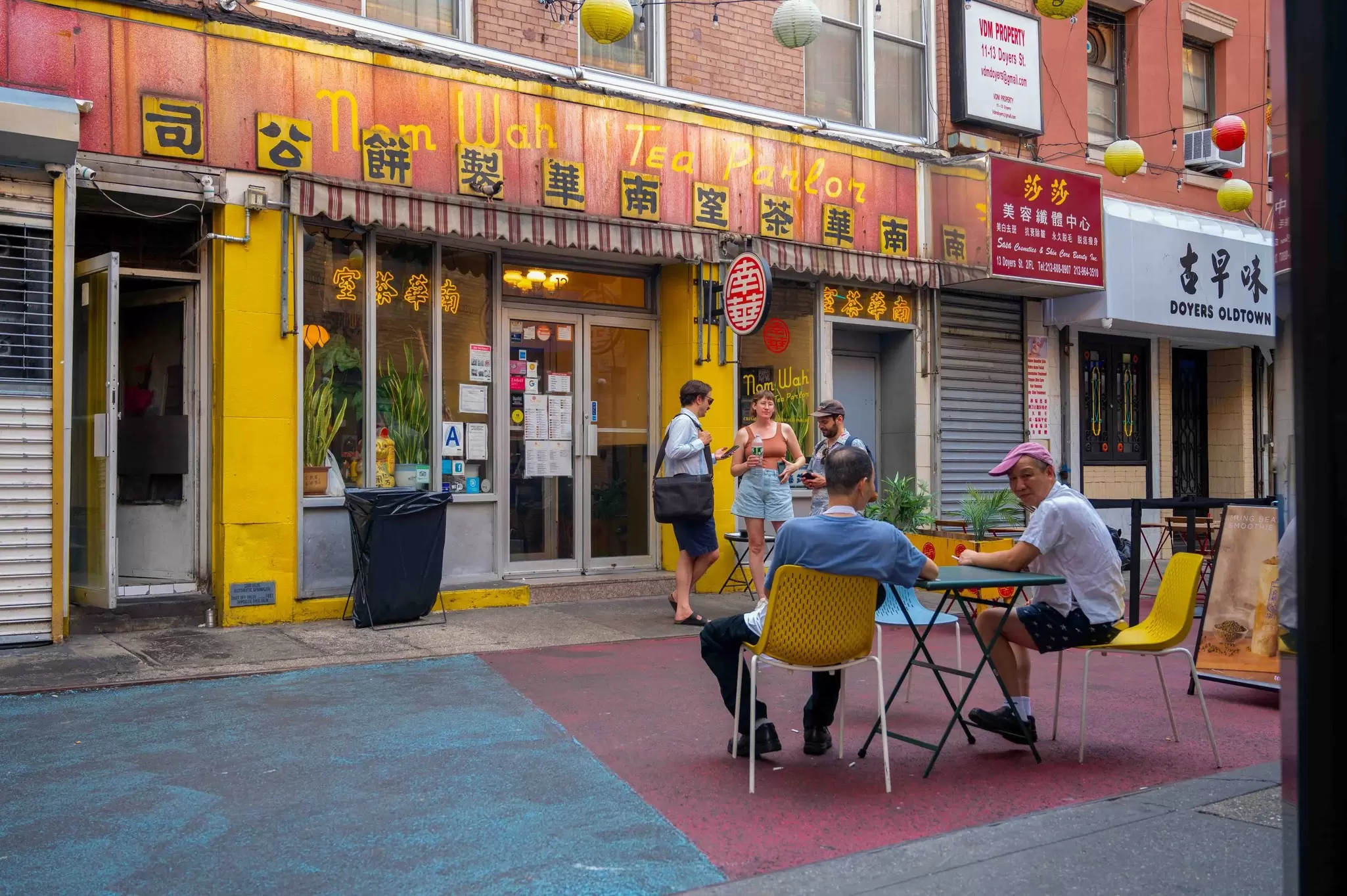 People at an outdoor restaurant table in Chinatown NY Doyers St with colorful asphalt street in front of Nam Wa Tea Parlor.