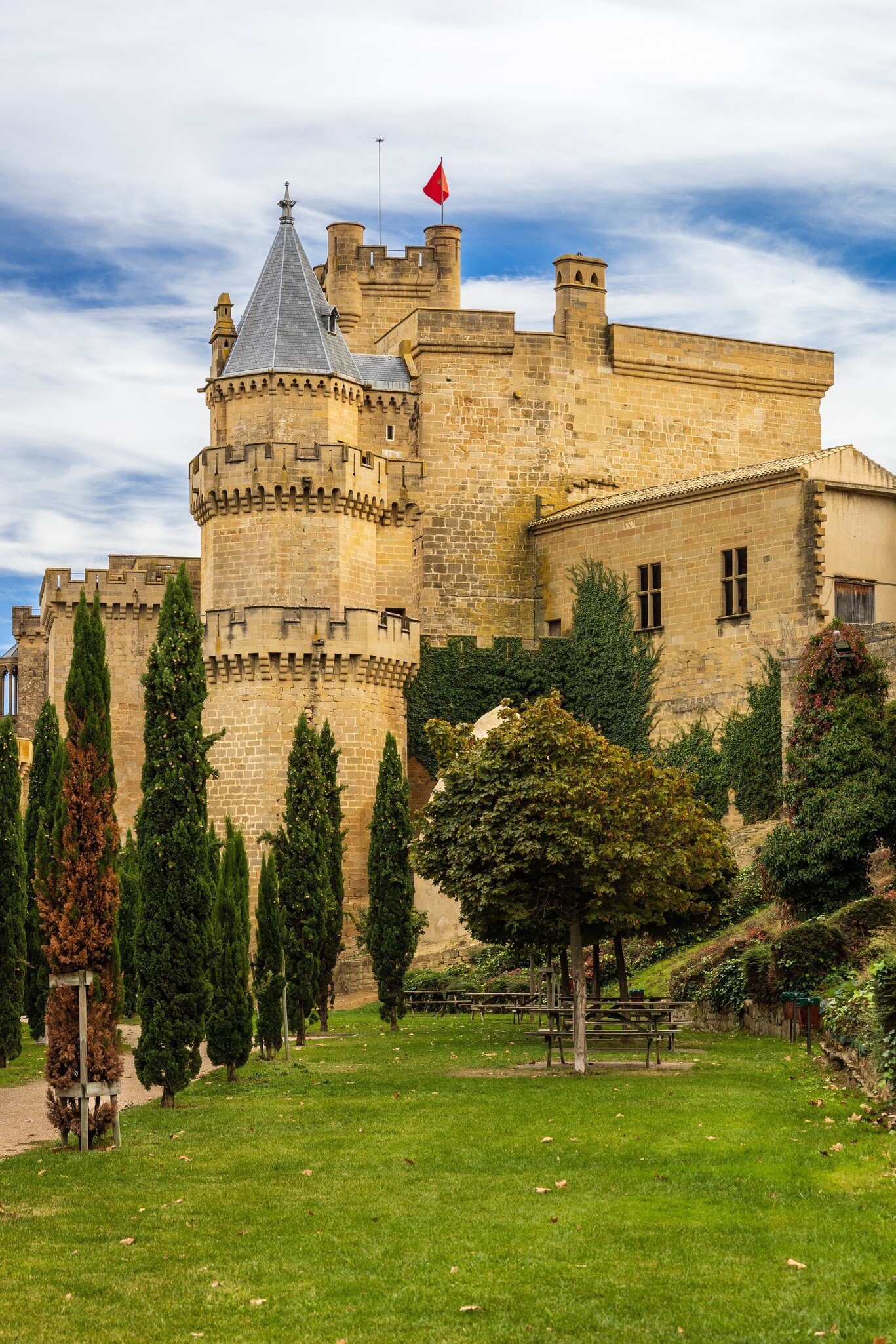 View of the Palacio Real in Olite, Spain, with a green lawn and cypress trees in the foreground.