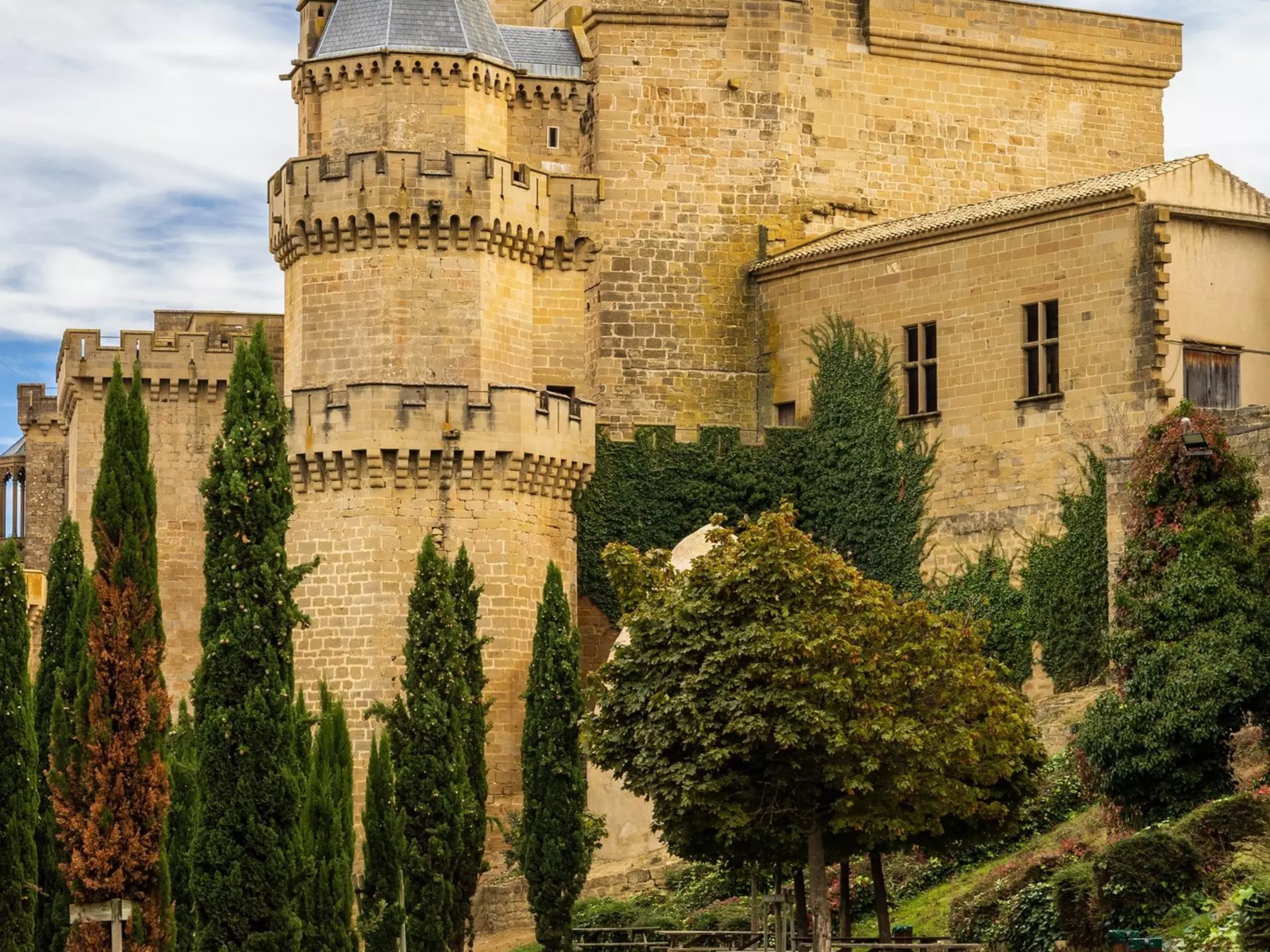 View of the Palacio Real in Olite, Spain, with a green lawn and cypress trees in the foreground.