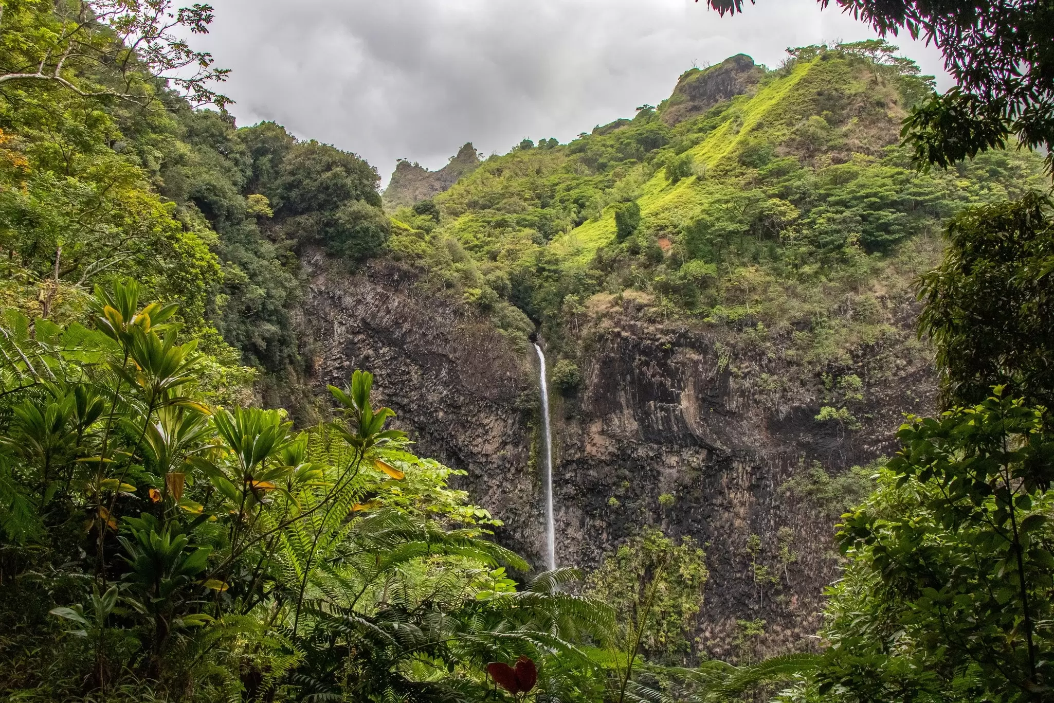 A tall, narrow cascade is pictured in a lush mountain valley, Tahiti, French Polynesia