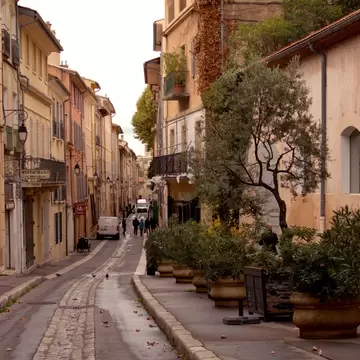 A narrow street of shuttered ocher facades and potted olive trees in Aix-en-Provence; signs read 'Restaurant'