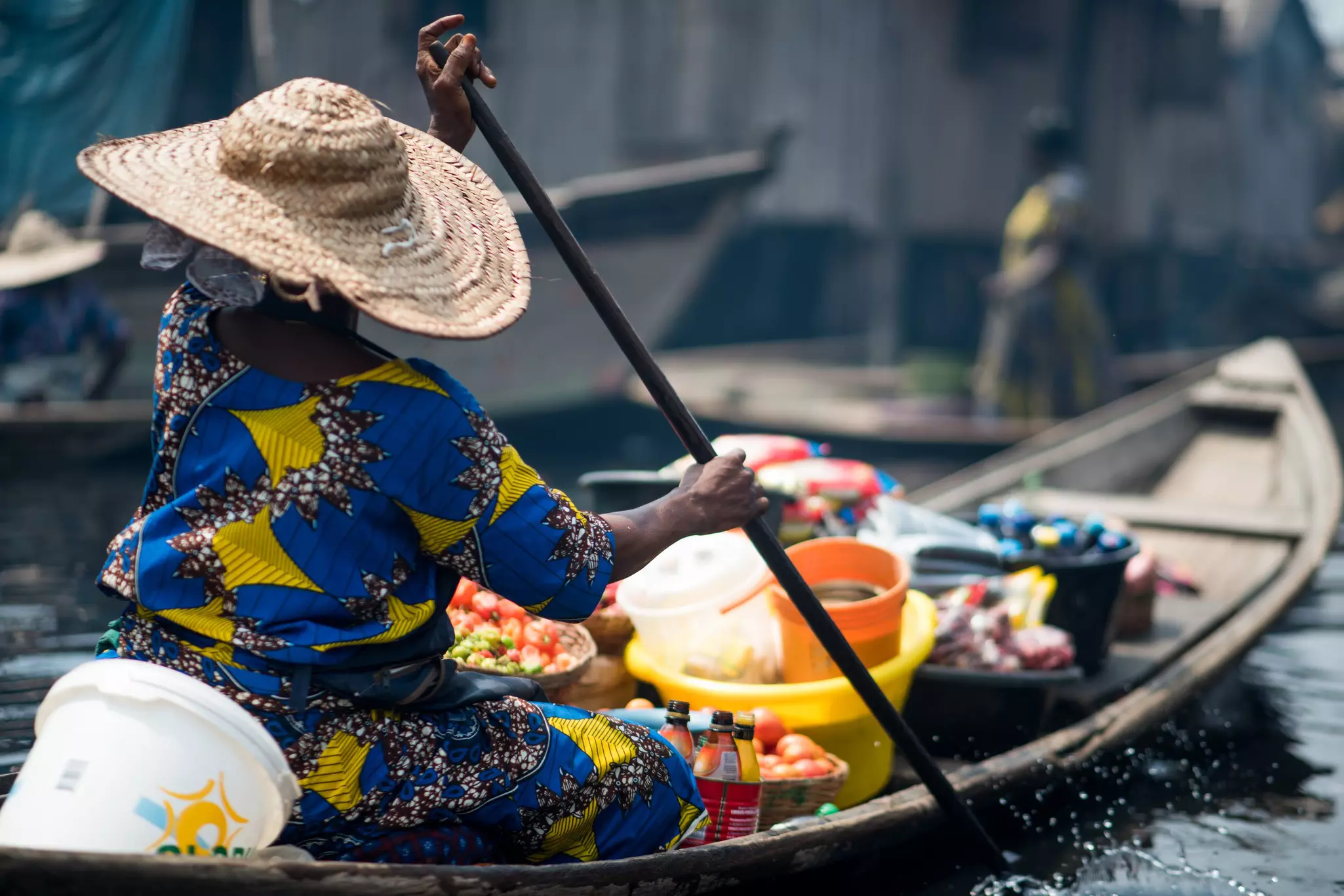 A person paddles a boat with goods in the bow.