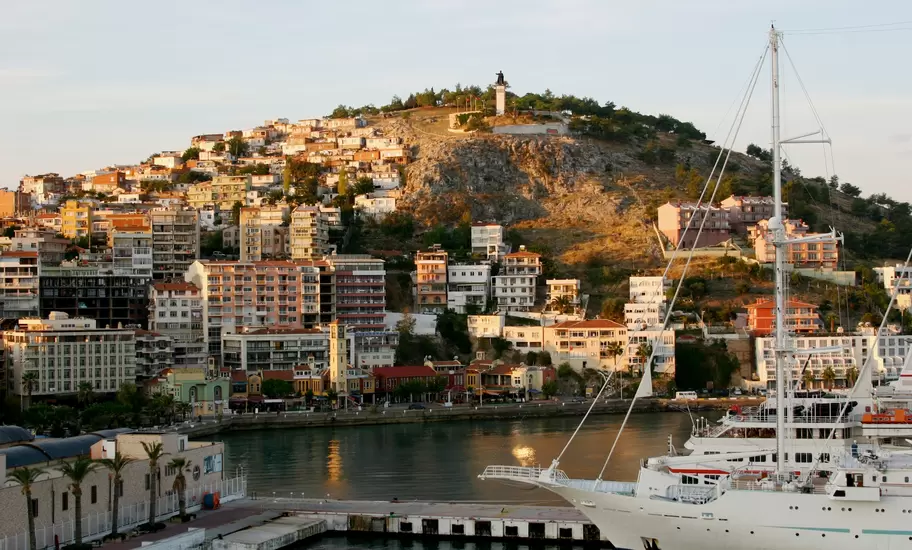 Kuşadası, Turkey: hillside of apartments rising to a rocky hilltop statue, a sailing cruise ship moored in the harbour
