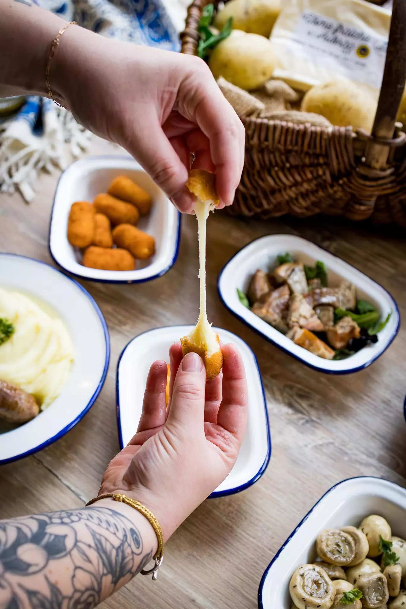 Two hands break apart a cheesy croquette stretching the melted cheese to form a string between the two parts.