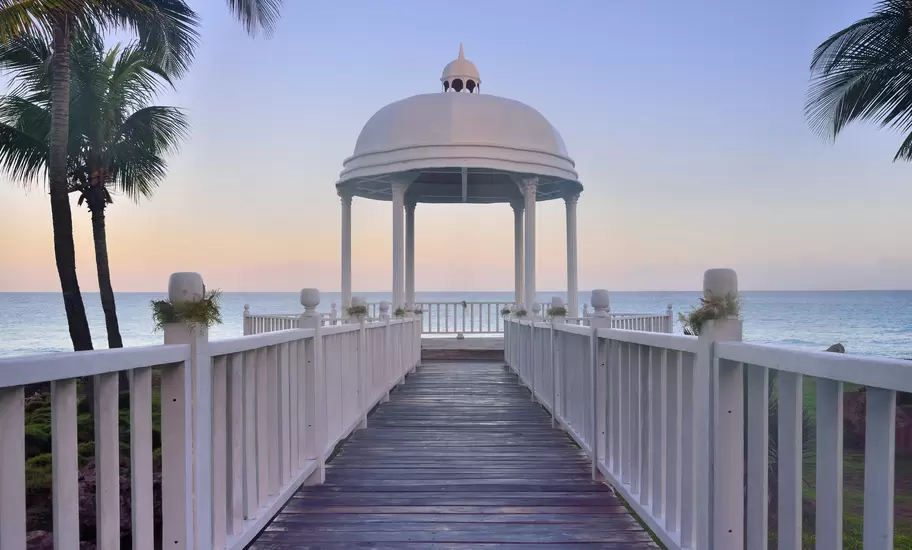 White domed gazebo at the end of a railed boardwalk overlooking the sea, framed by palms at dusk in Varadero