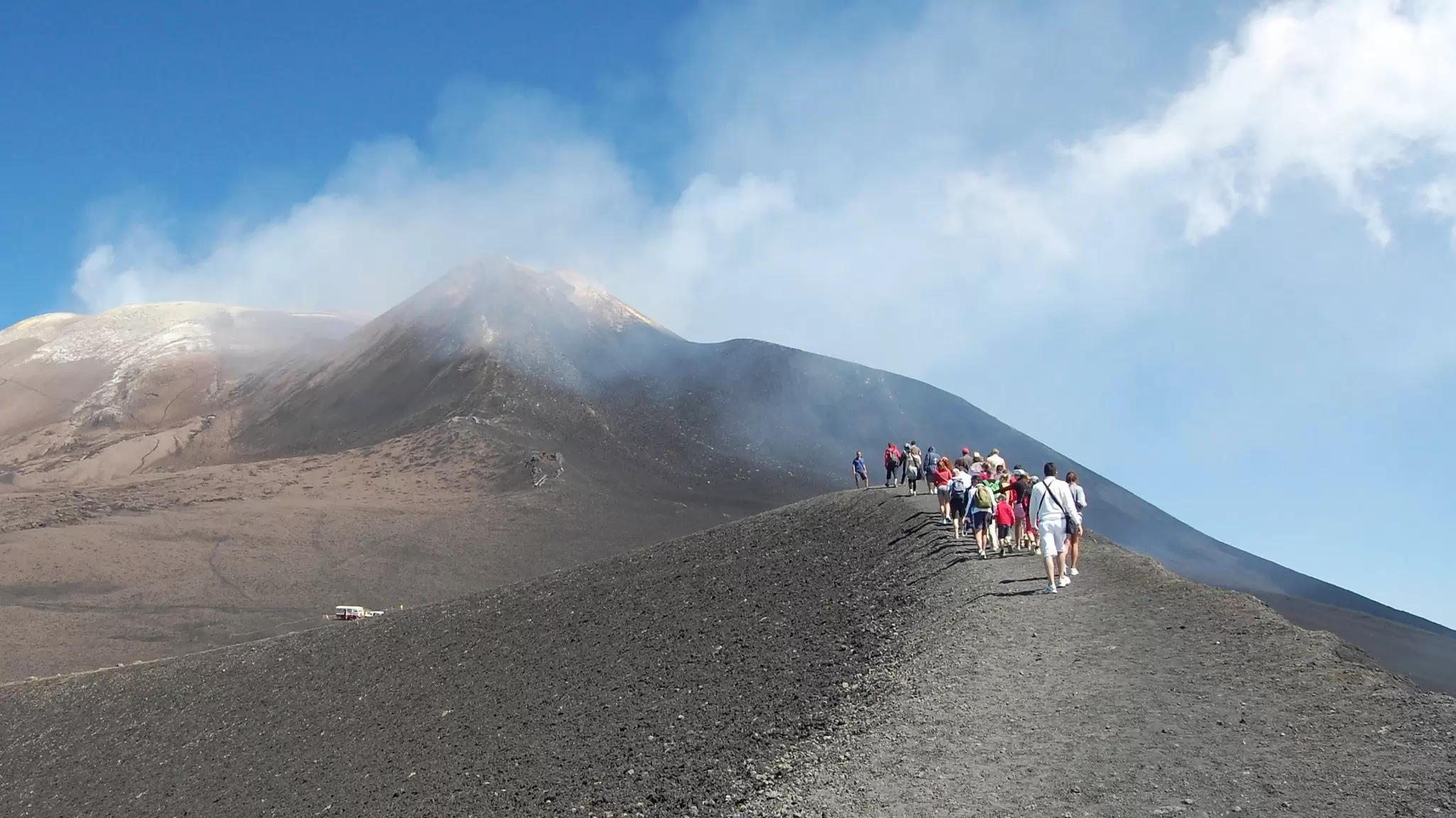 A group of hikers in a single line climbing a smoking Mt Etna, Sicily, Italy.