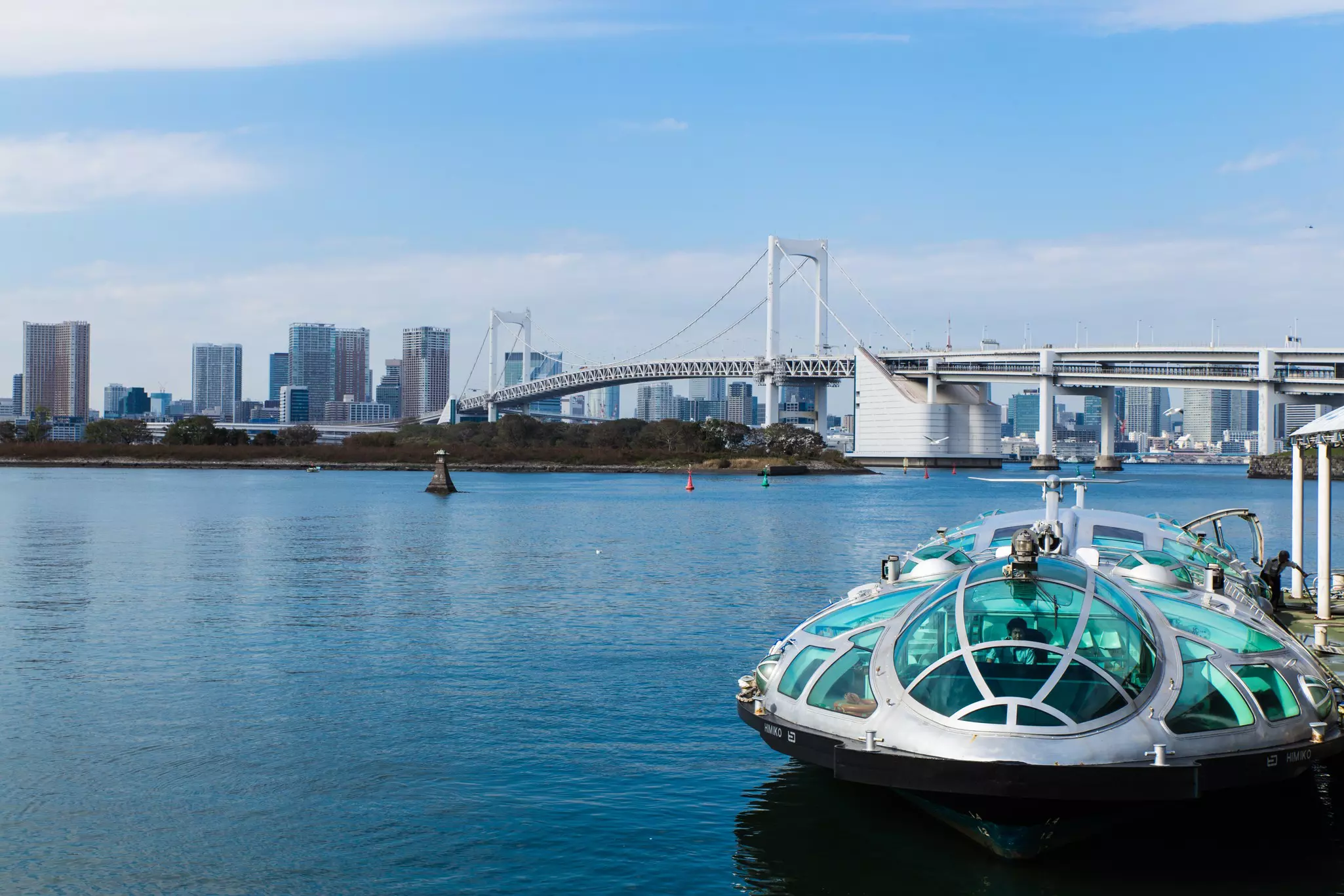 A spaceship-like, metal and glass vehicle docked over water. A bridge is in the background.