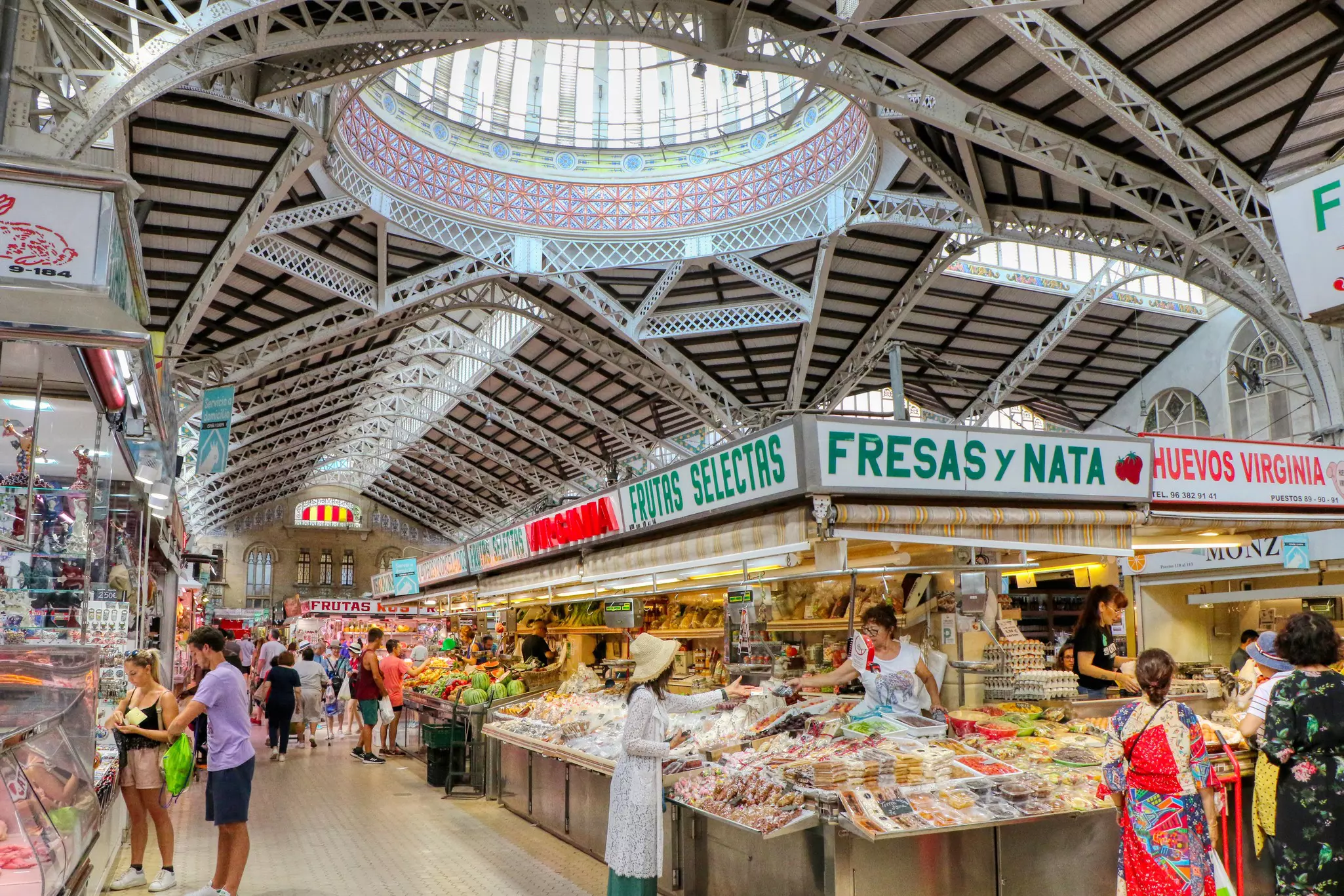 People line up at greengrocer stalls in an indoor market to purchase food