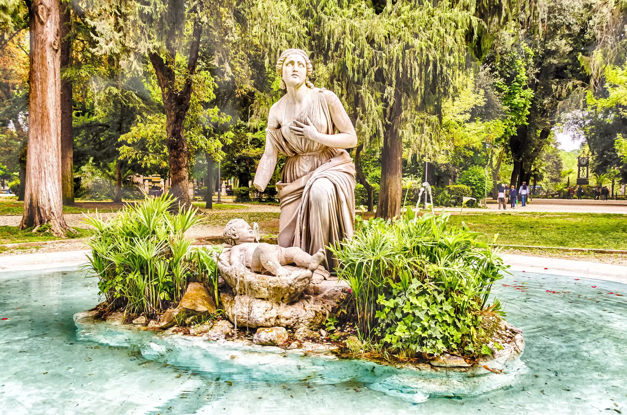 A statue is the centerpeice of a fountain in parkland