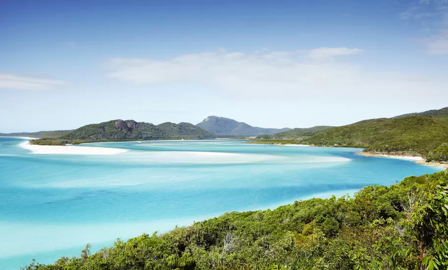 A vast bay near a tropical island with turquoise waters and bright white sands.