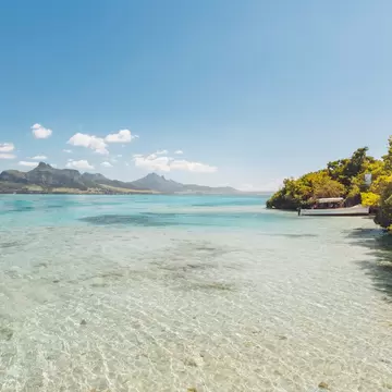 Clear turquoise shallows over pale sand running to a reef edge, wooded shore alongside.