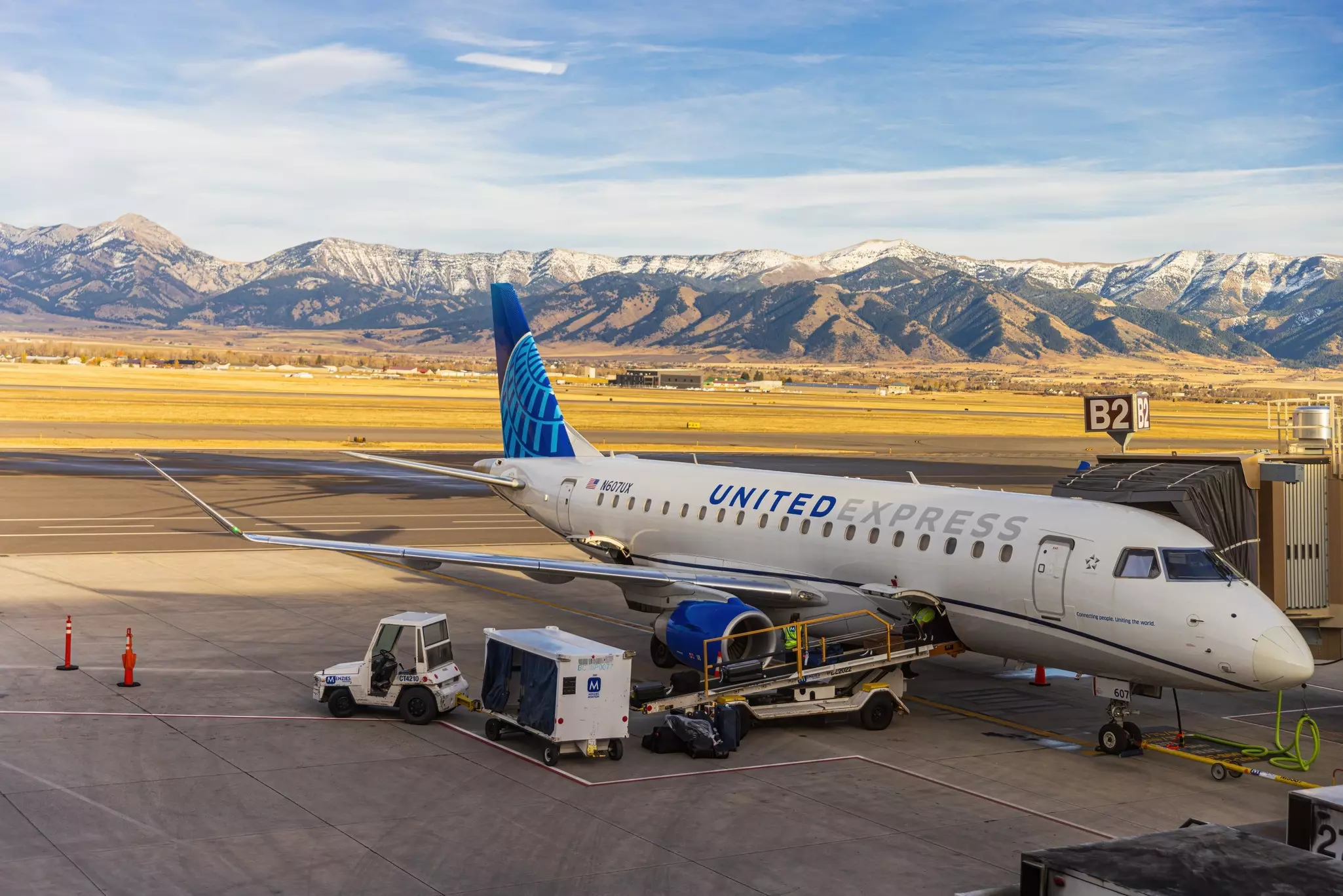 An airplane parked at its gate with the runway and mountains in the background