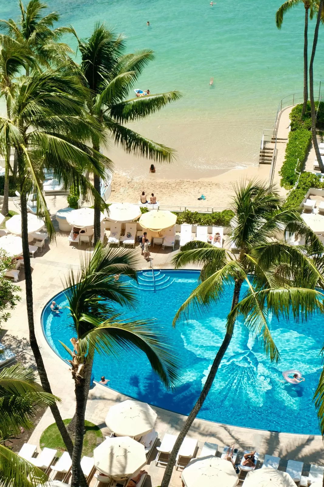 A gorgeous blue swimming pool just off the edge of a sandy beach.