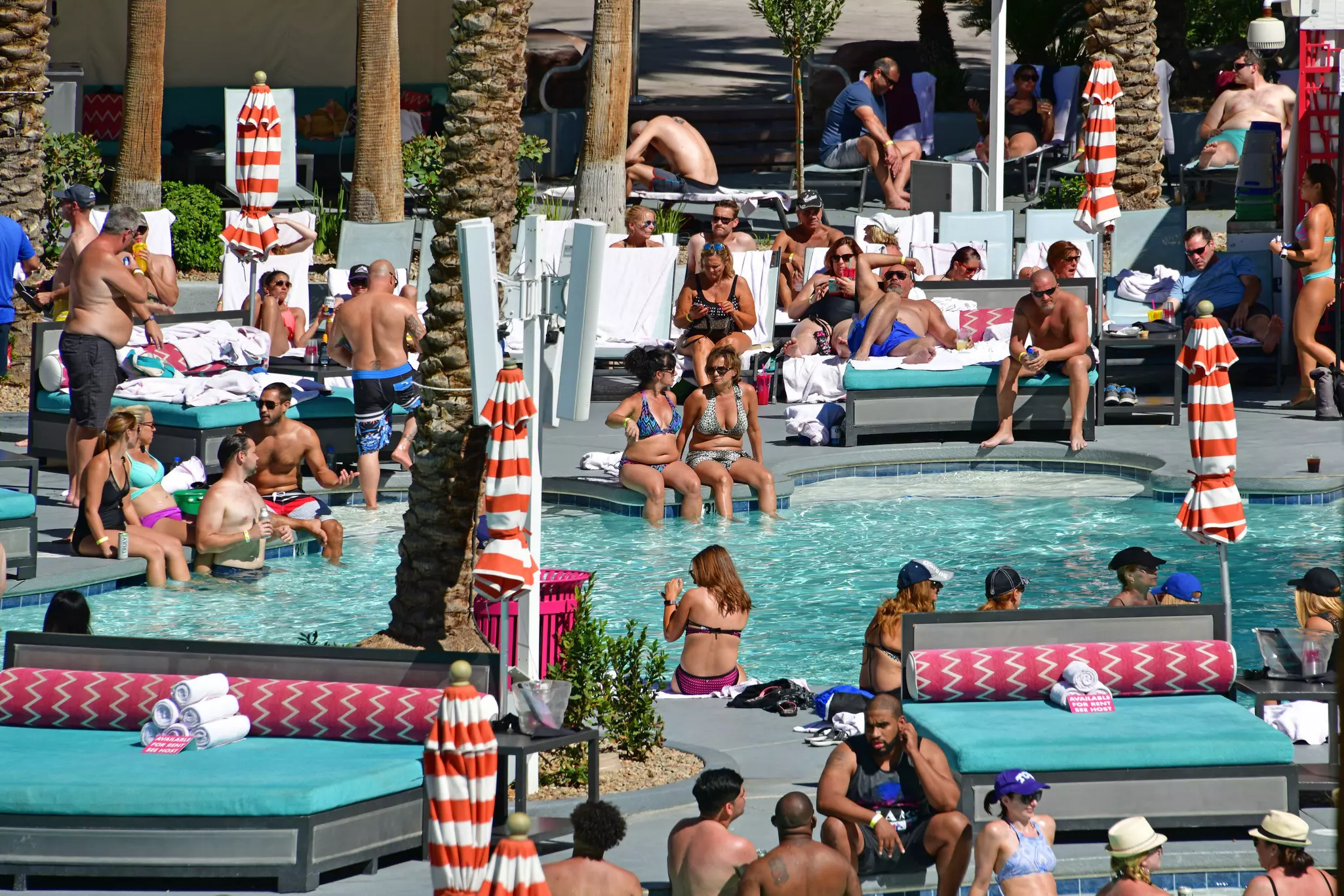 Numerous people cluster in and around a pool at a resort on a hot day.
