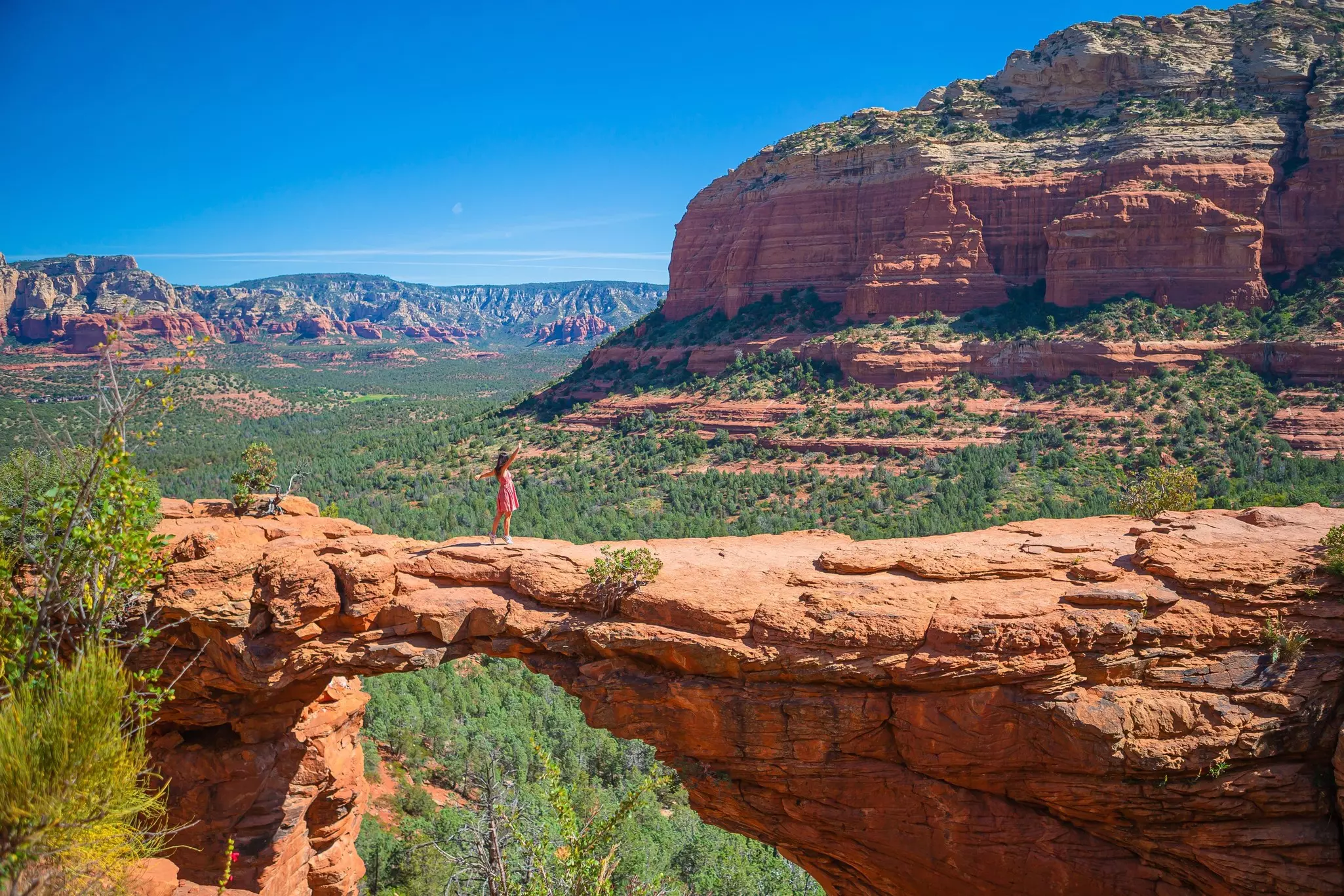 A woman standing on Devil's Bridge Trail with her arms raised in the air.