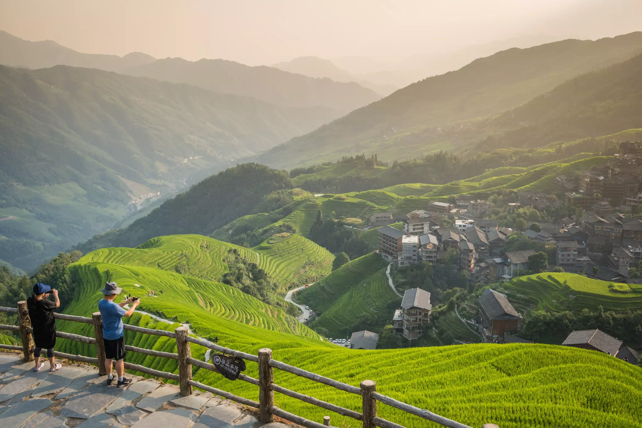 People at a viewpoint over rolling rice paddies and a village below.