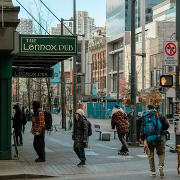 People standing, walking, and skateboarding on the intersection of Granville and Robson streets, outside the Lennox pub. Vancouver, Canada.