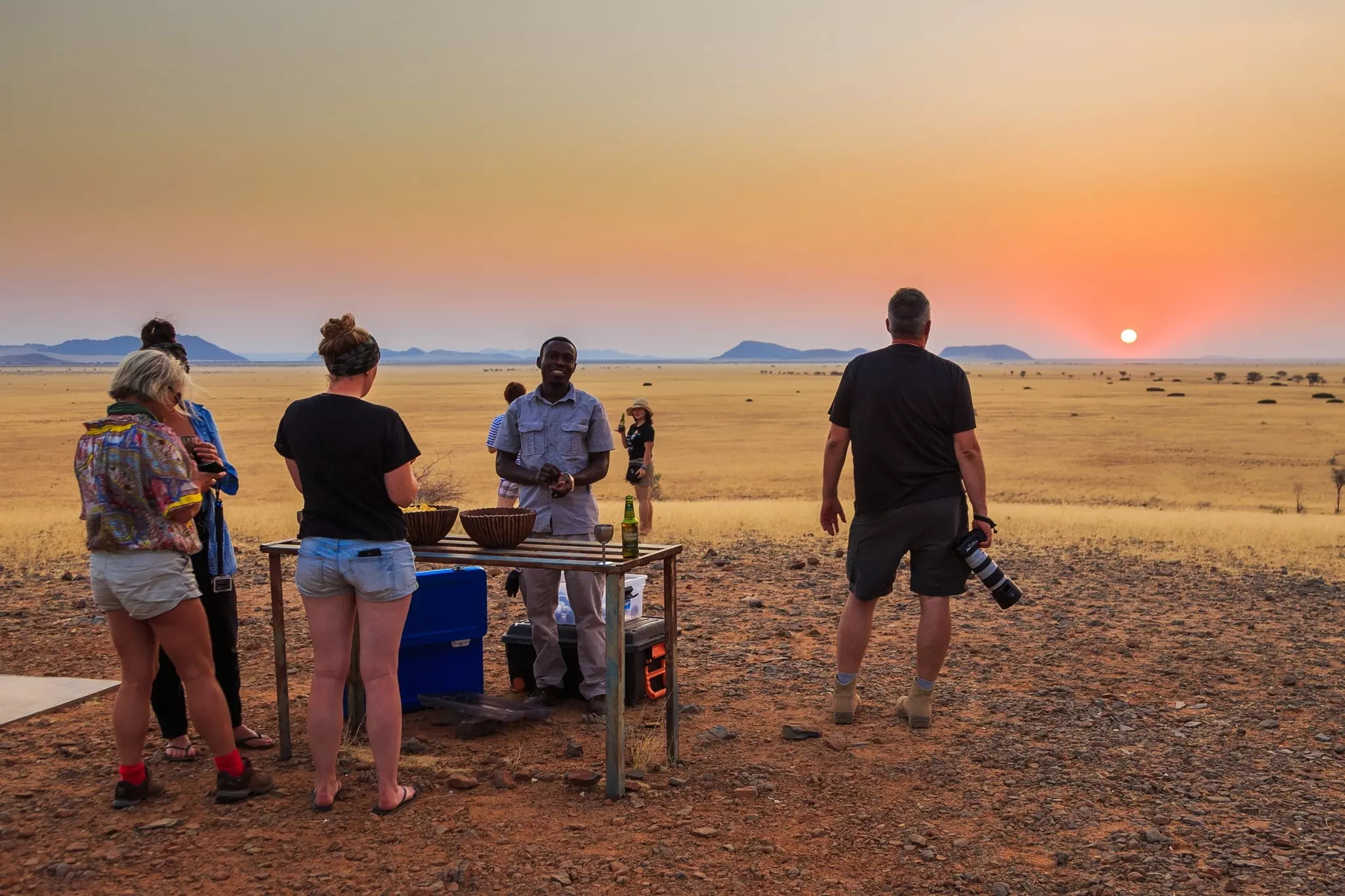 Solitaire, Namibia - 01 October 2018: Refreshments for safari. Tourists at the table. Sunset over the savannah in the background. Beautiful landscape., License Type: media, Download Time: 2025-02-07T16:31:41.000Z, User: rhylton_redventures, Editorial: true, purchase_order: 65030 - Newsletter, job: Lonely Planet WIP, client: Lonely Planet WIP, other: Rhianydd Hylton