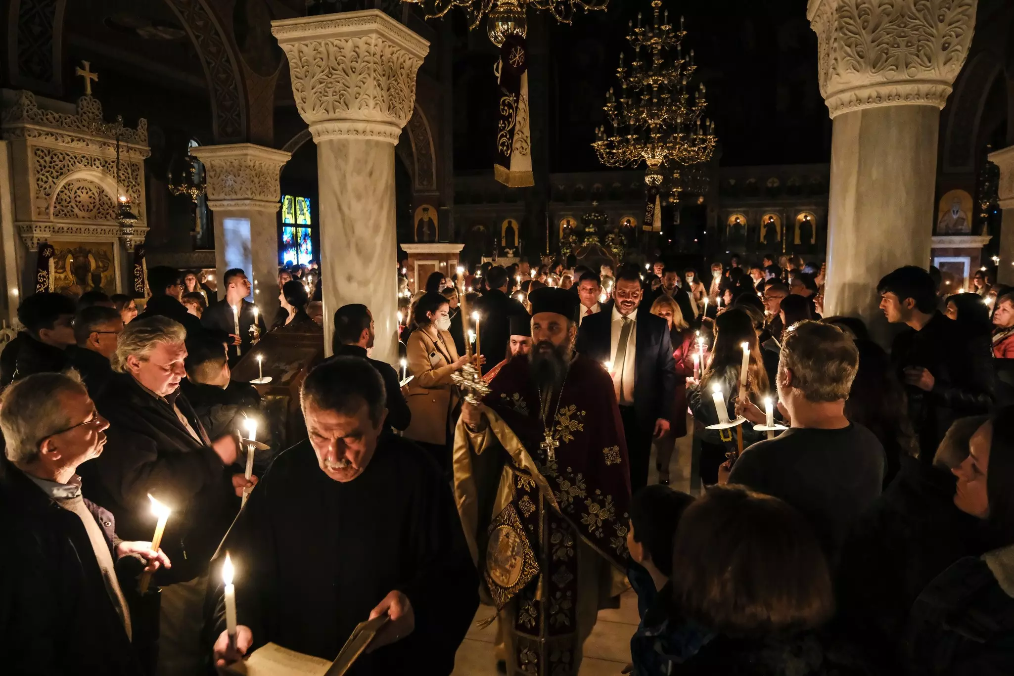 People hold candles during a religious service in the darkened interior of a church.