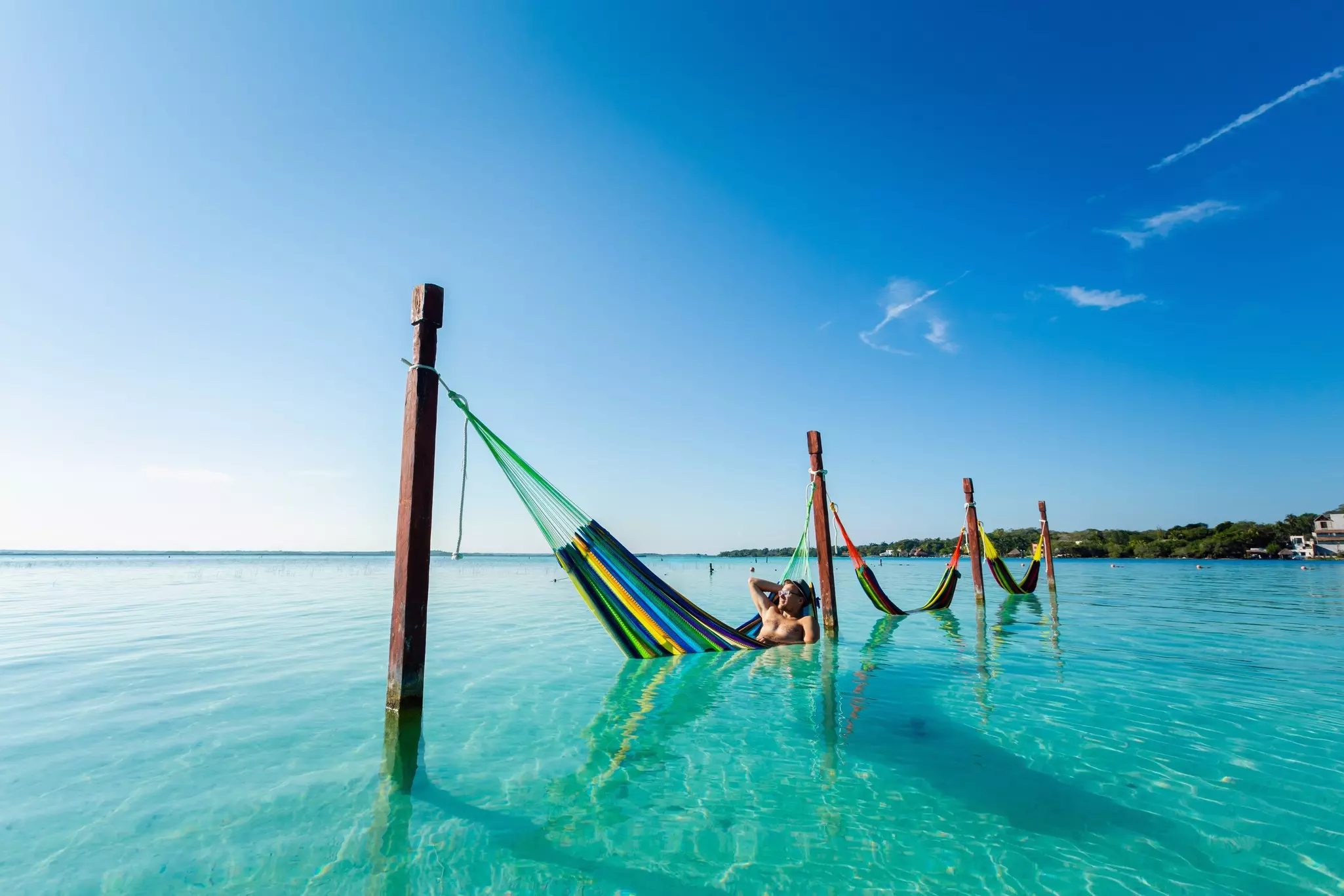 A person rests in a hammock placed in the water in a tropical lagoon.