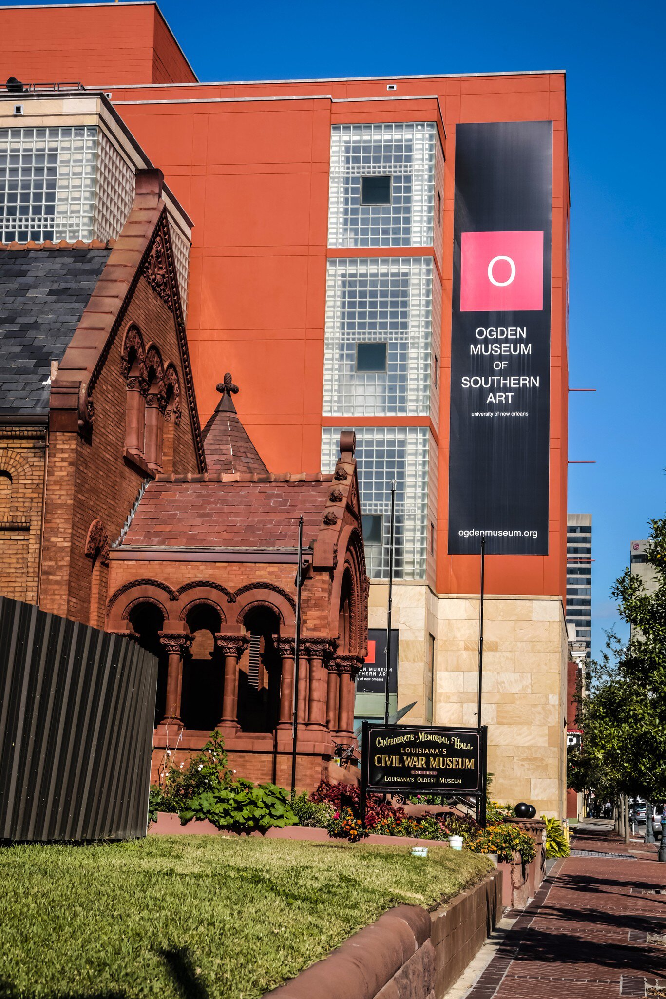 Black banner reading 'Ogden Museum of Southern Art' on an orange wall beside red-brick Confederate Memorial Hall.