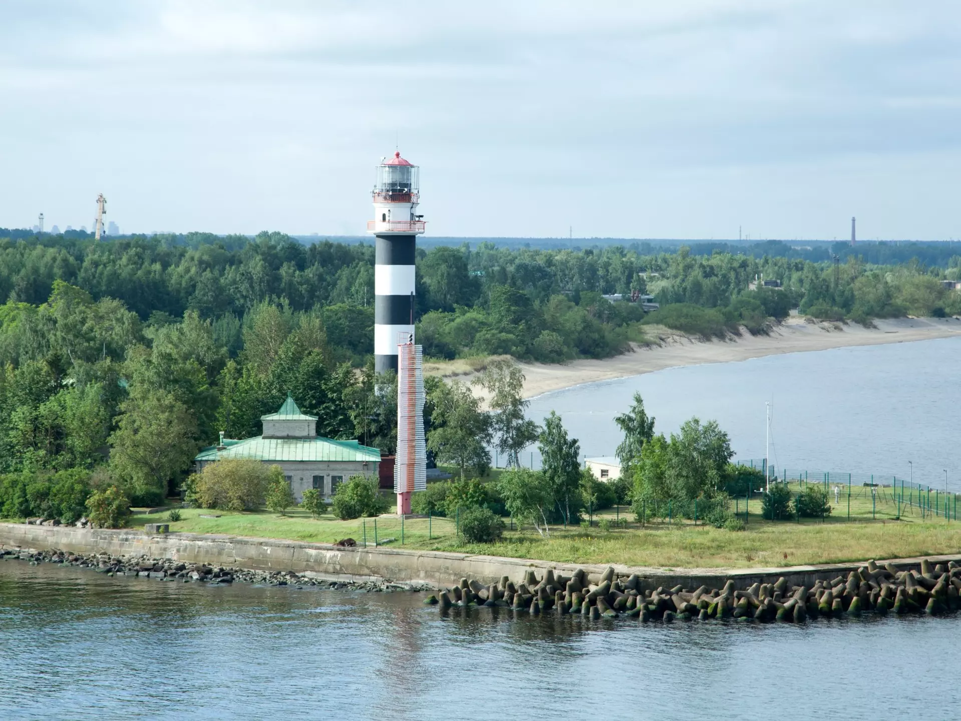 An aerial view of a lighthouse painted black and white at a breakwater at the entrance to a port.