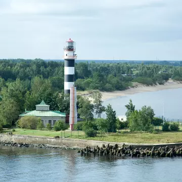 An aerial view of a lighthouse painted black and white at a breakwater at the entrance to a port.