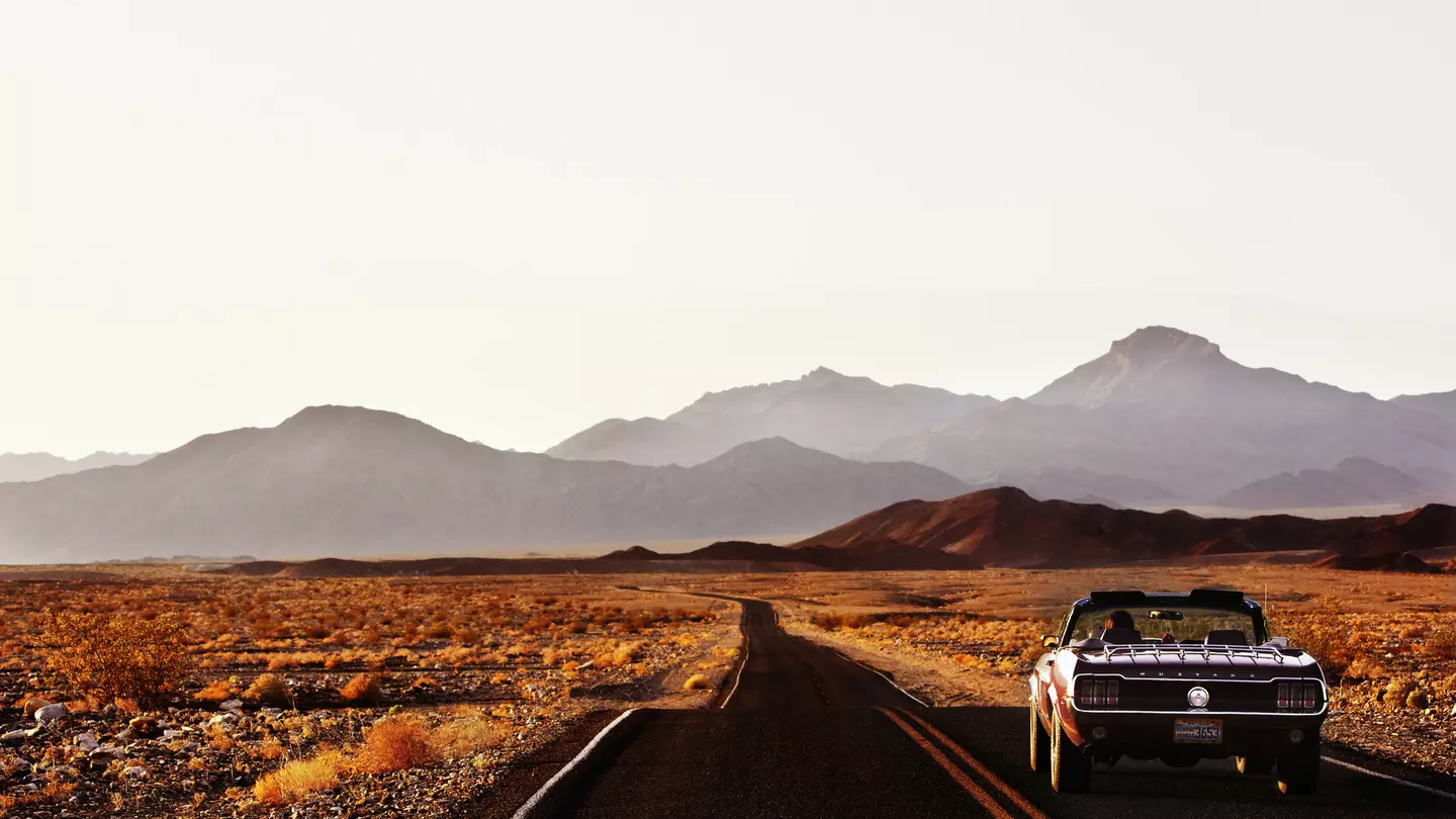 A car driving down a road through the desert landscape of Death Valley.