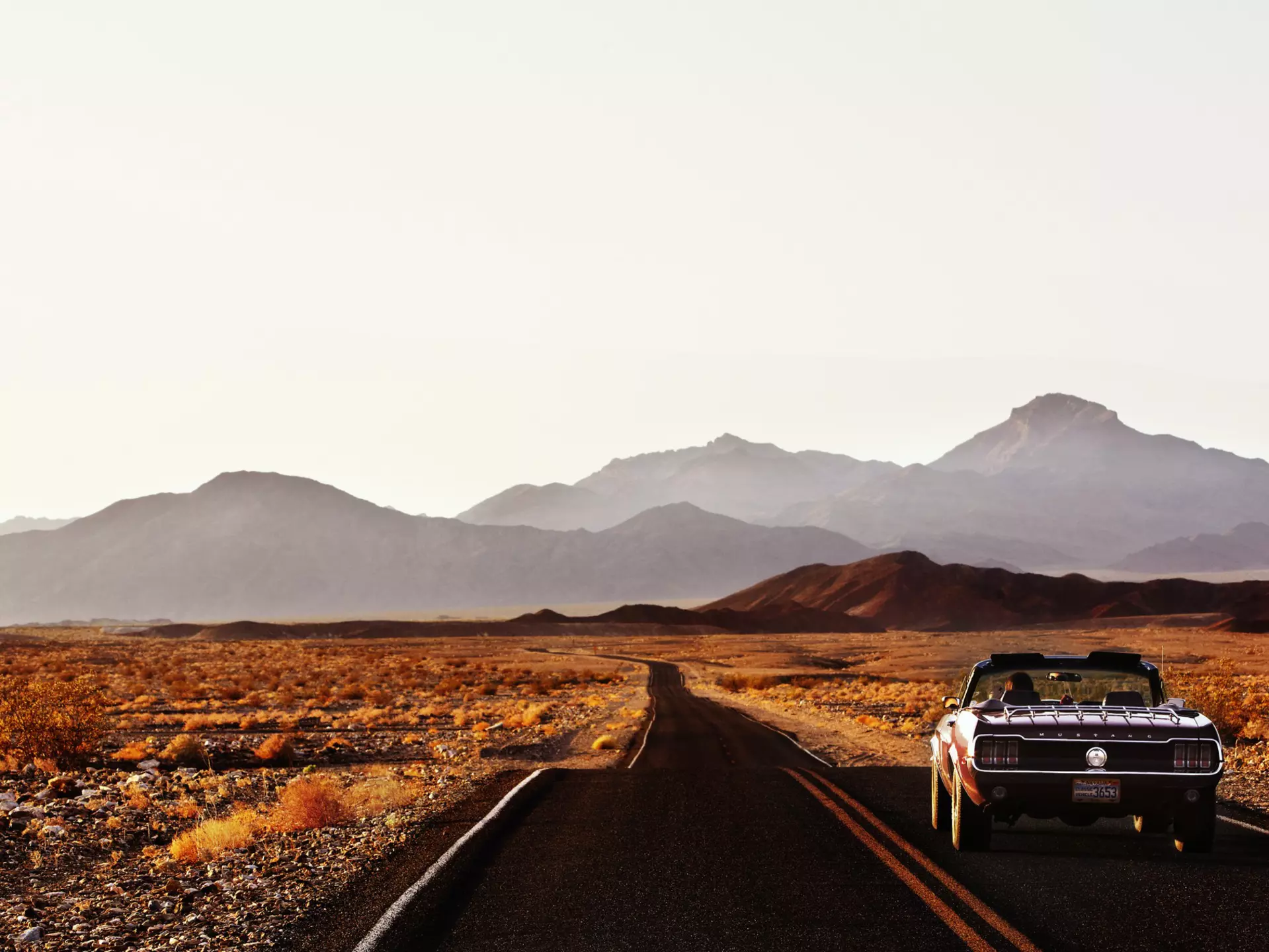 A car driving down a road through the desert landscape of Death Valley.