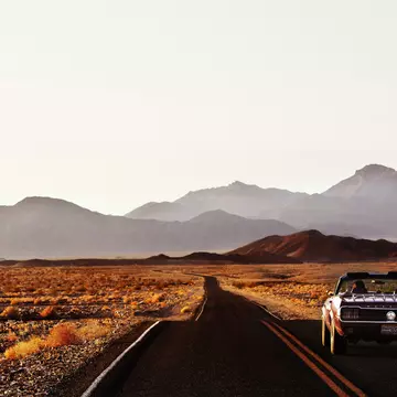 A car driving down a road through the desert landscape of Death Valley.