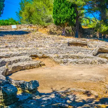 Rock-cut semicircular seating tiers of a small Roman theatre surrounded by pine trees.