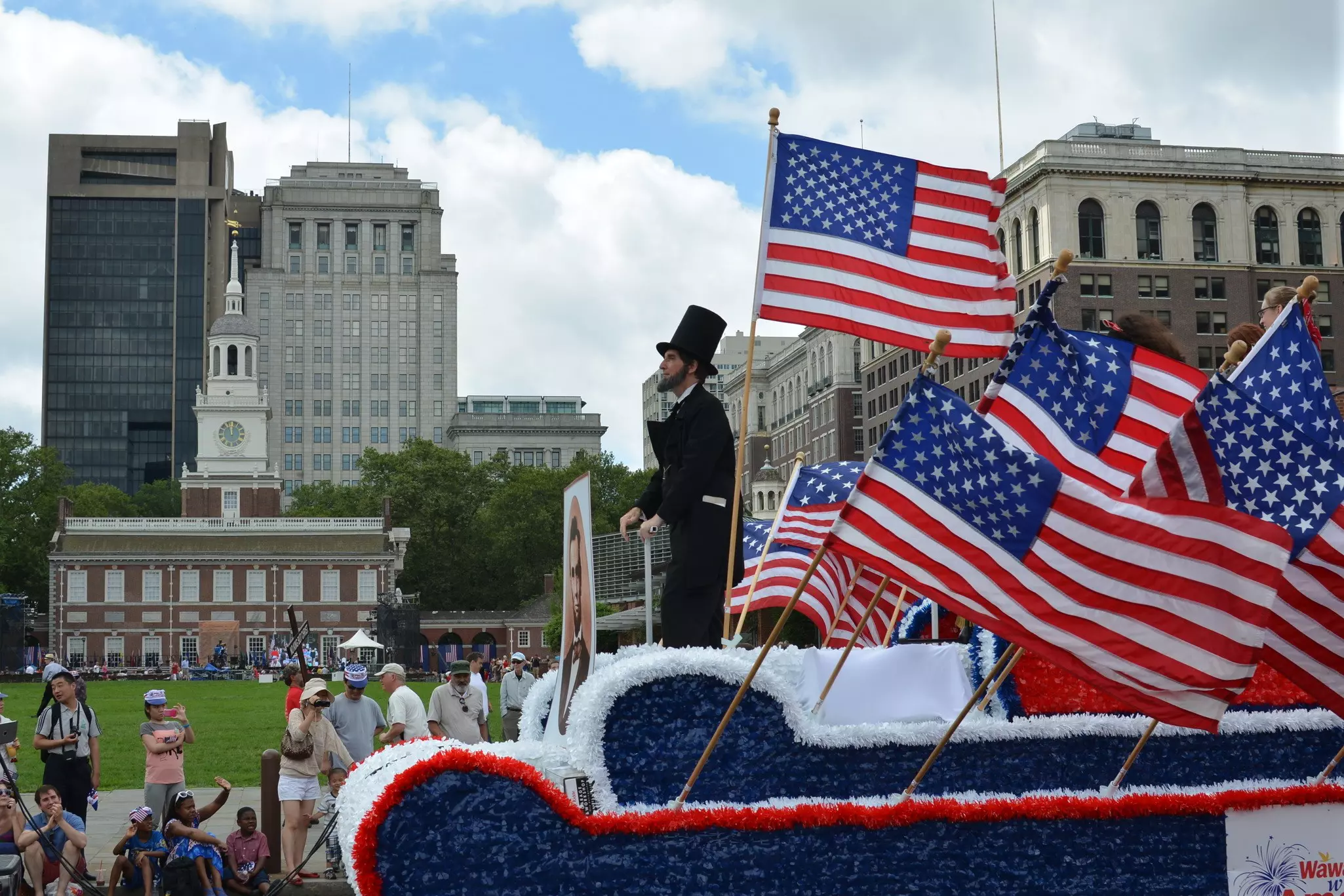 Man dressed as Abraham Lincoln rides a float full of American flags in an Independence Day parade