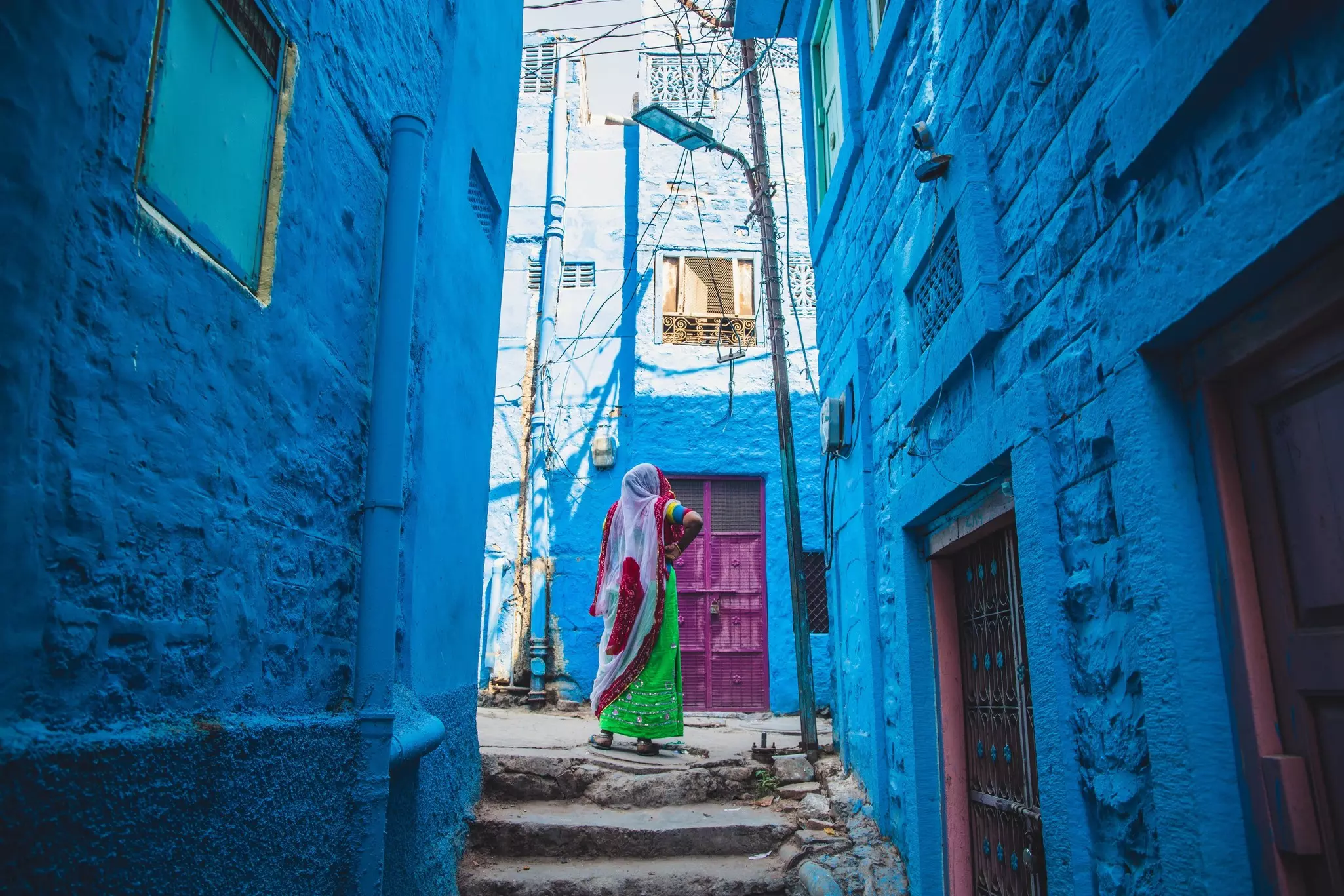 A woman standing in an alley with all surrounding buildings painted blue in Jodhpur