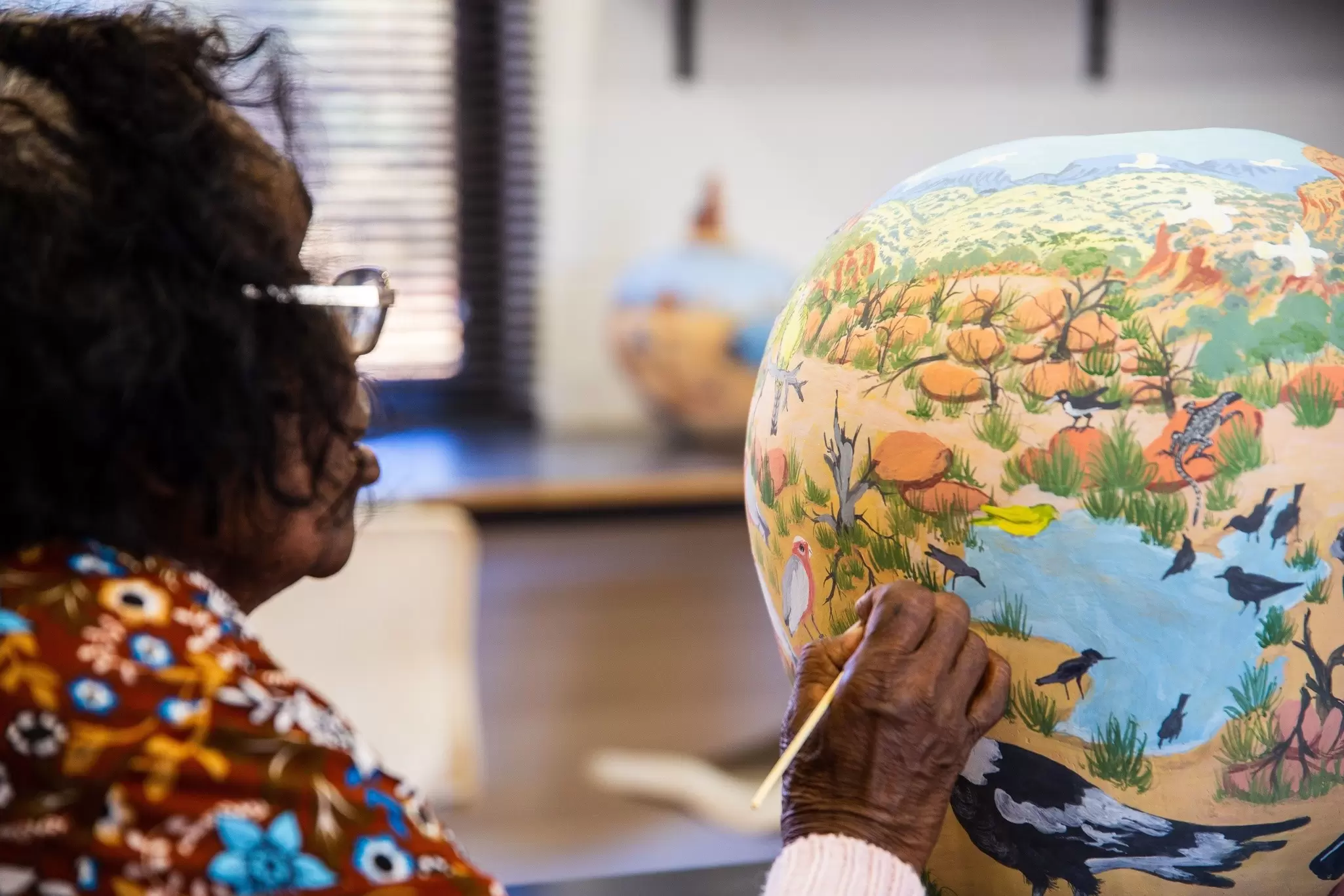 An Aboriginal artist is painting a colorful pot at Hermannsburg, near Alice Springs.