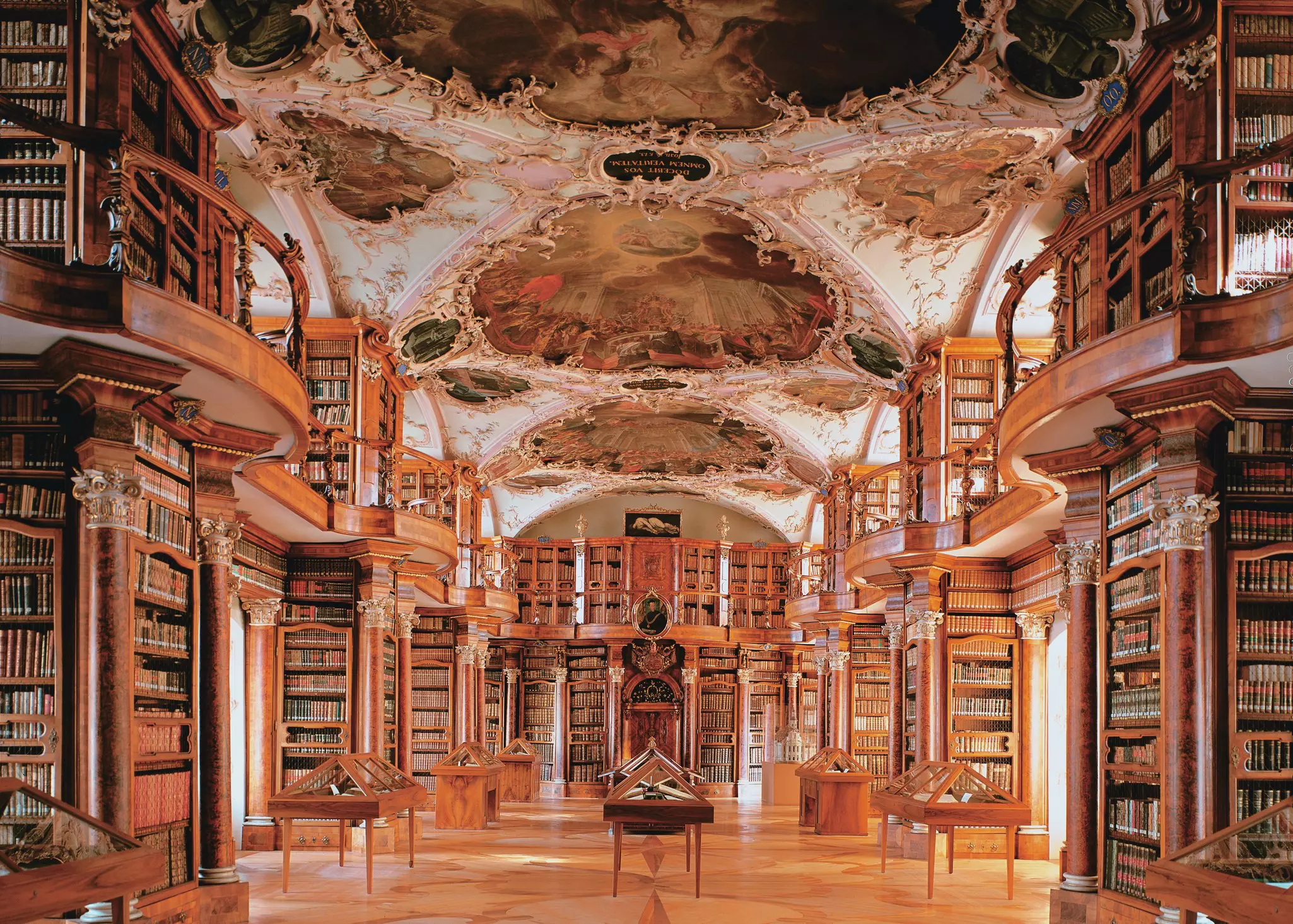 An ornate, historic library with curved bookshelves and a painted ceiling
