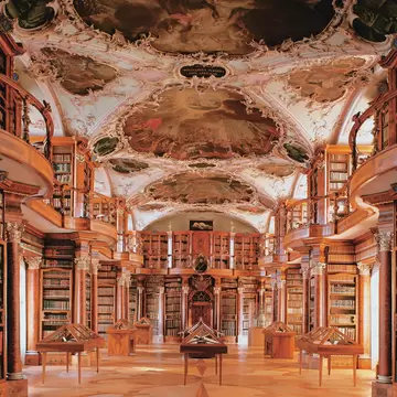 An ornate, historic library with curved bookshelves and a painted ceiling