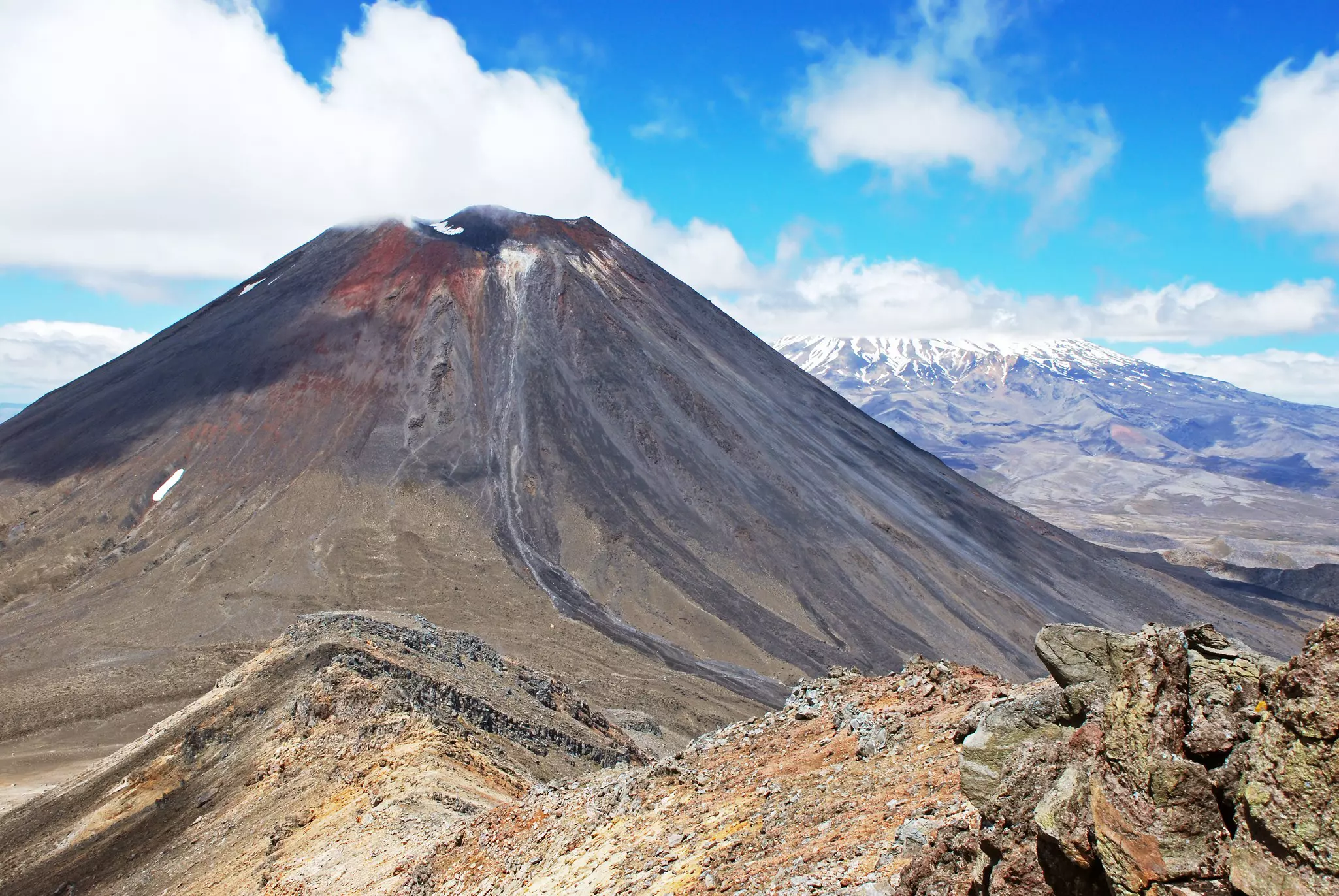 A volcanic mountain peak with snow-capped mountains in the distance