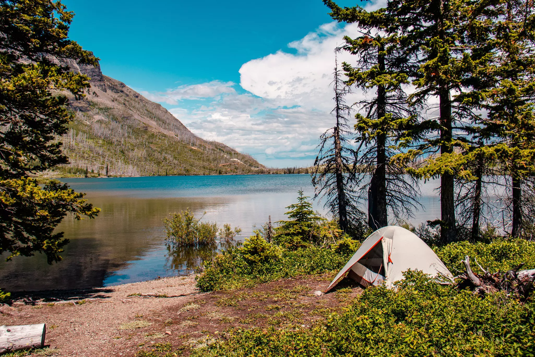 A tent pitched at the edge of a mountain lake on a sunny day