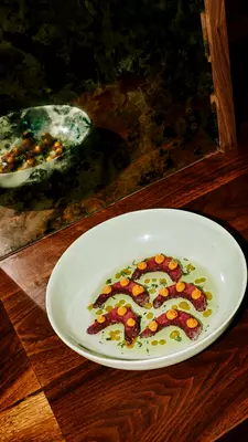 A white bowl with five shrimp topped with an orange sauce reflected in a mirror.