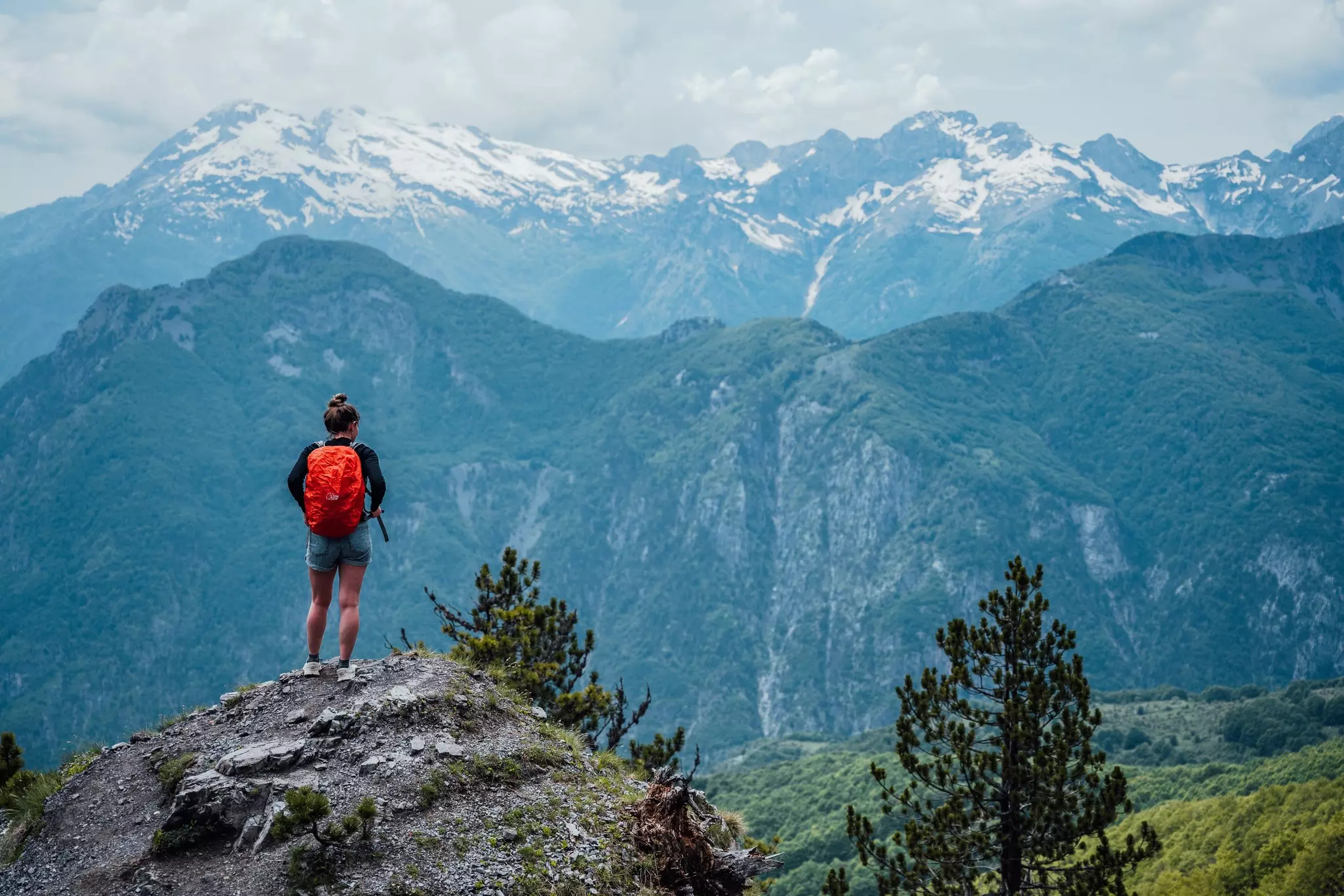 A hiker is seen from behind standing on a rock looking out at valley and mountains beyond.