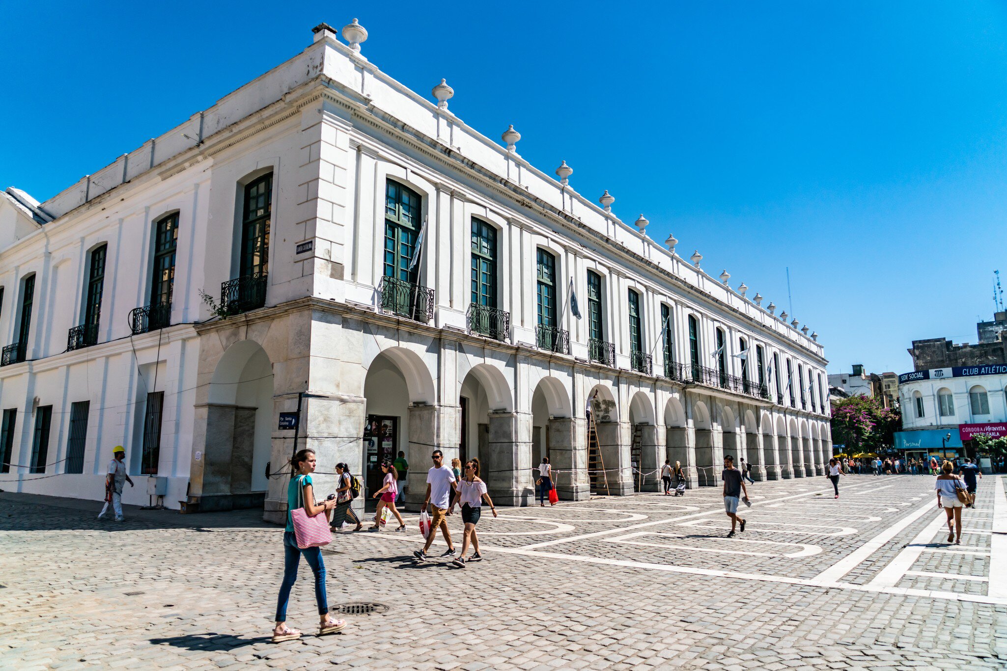 Locals and tourist passing a colonial building at the Plaza San Martin in the center of town. Cordoba, Argentina.