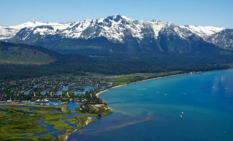 Aerial view of South Lake Tahoe's Tahoe Keys marina, marshland and beach beneath snowcapped Mt Tallac on Lake Tahoe