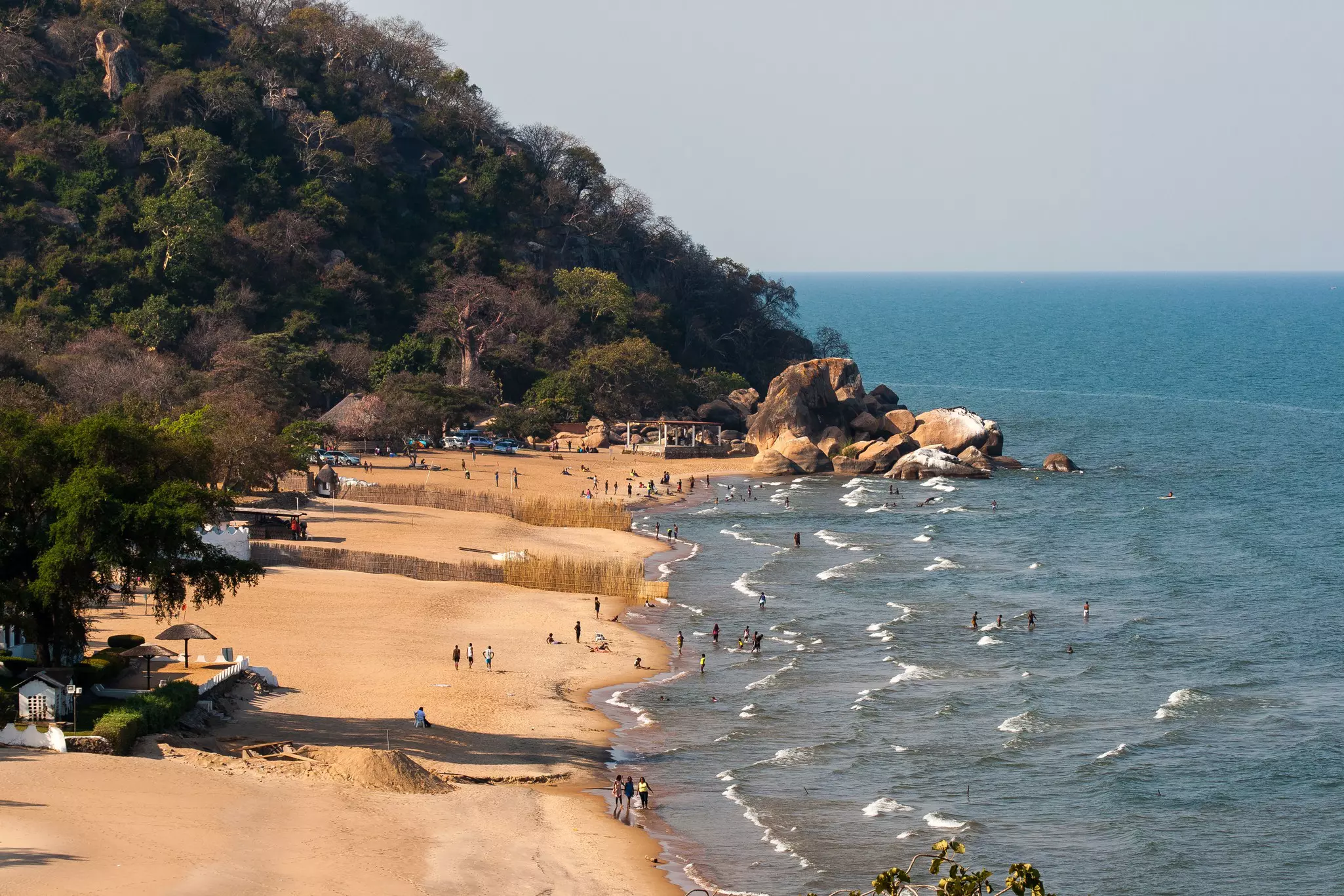 A wide view of people swimming in waves on a beach by a lake.
