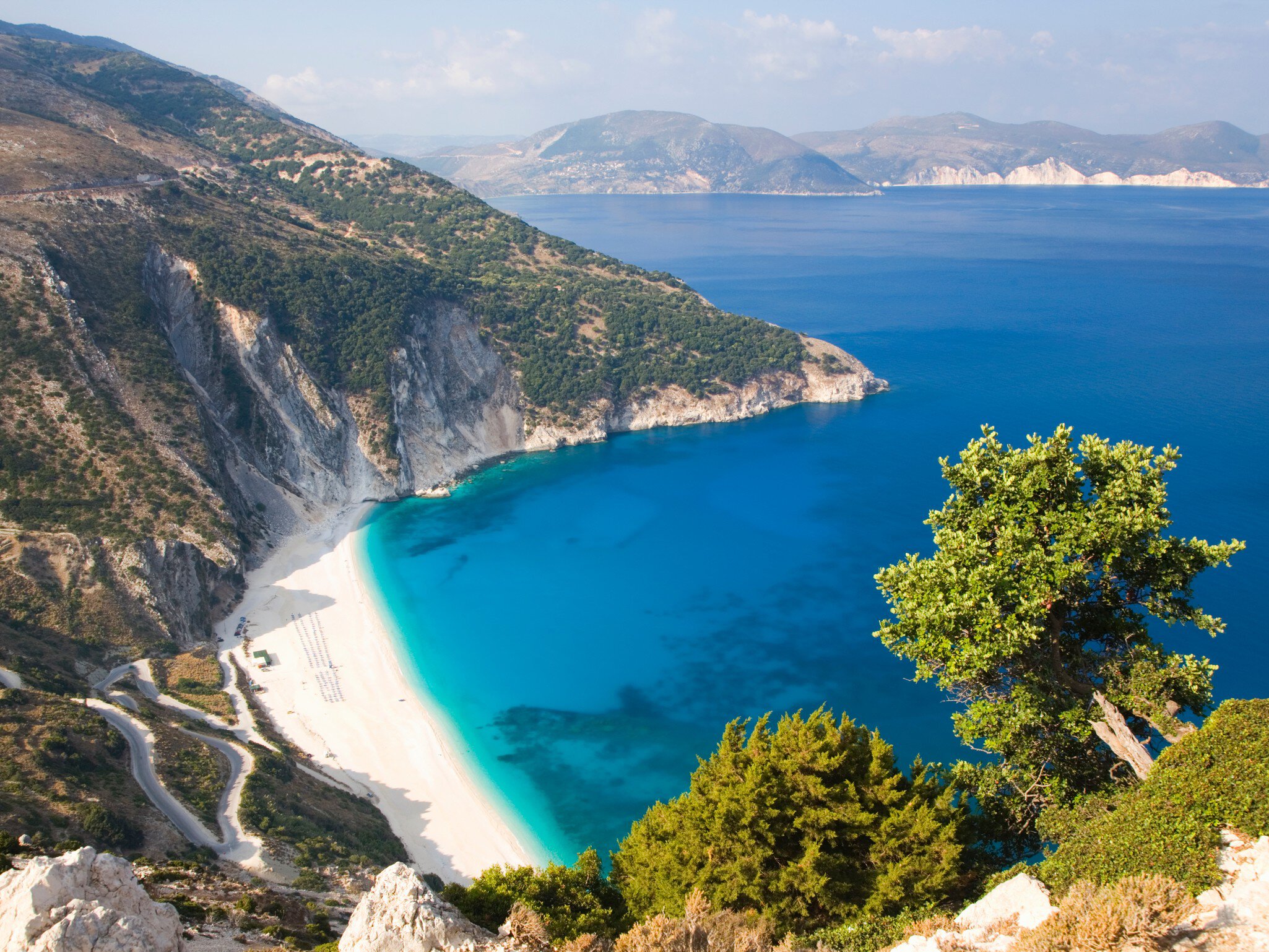 A curve of white sand below steep cliffs. The calm turquoise sea laps at the shore.