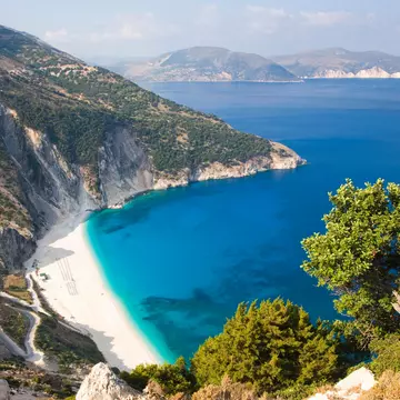 A curve of white sand below steep cliffs. The calm turquoise sea laps at the shore.