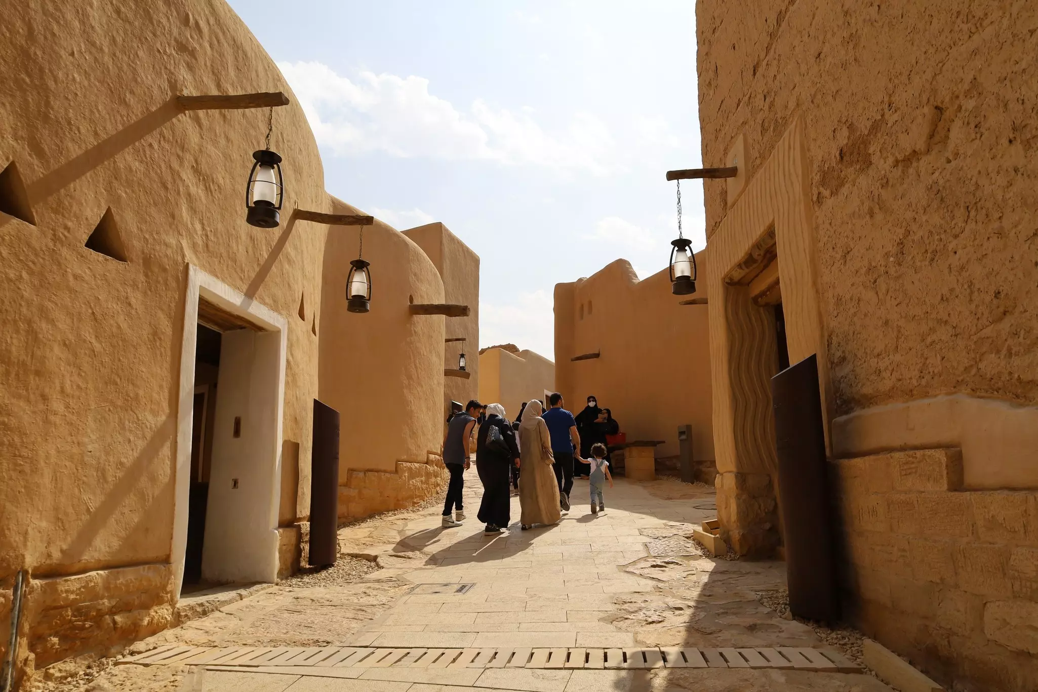 People walking past historic mud-brick houses in Diriyah, Saudi Arabia. 